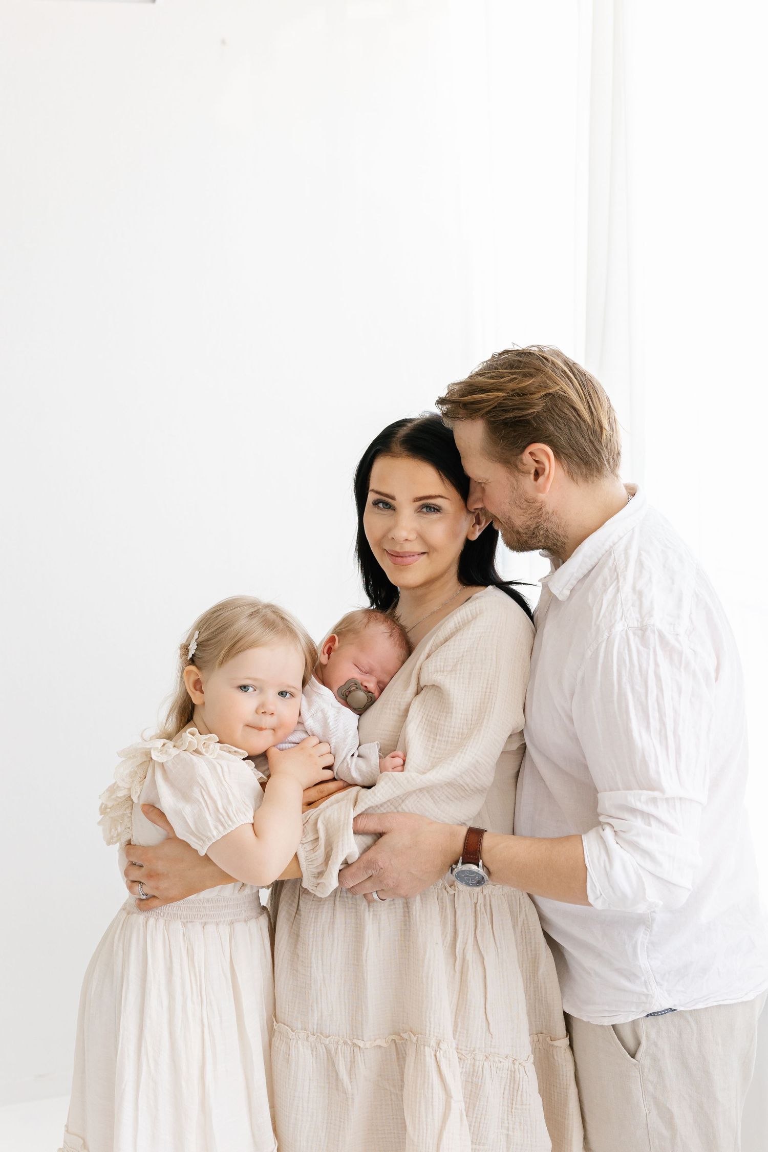 A family in white outfits shares tender moments together against a bright white background.