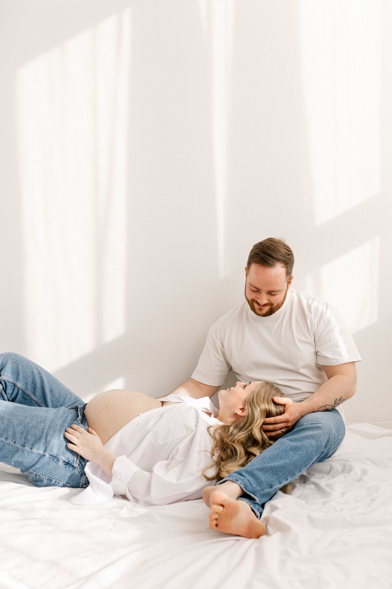 A series of intimate photos showing tender moments between a couple relaxing on a white bed in casual attire.