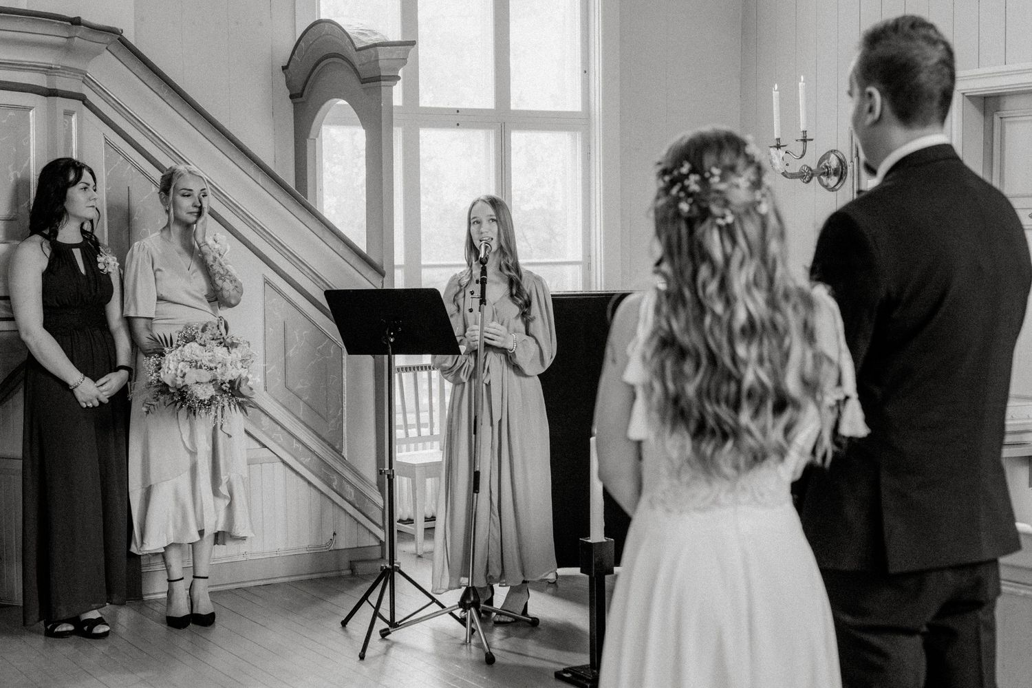Black and white photo of a wedding ceremony with musicians performing in an elegant interior.