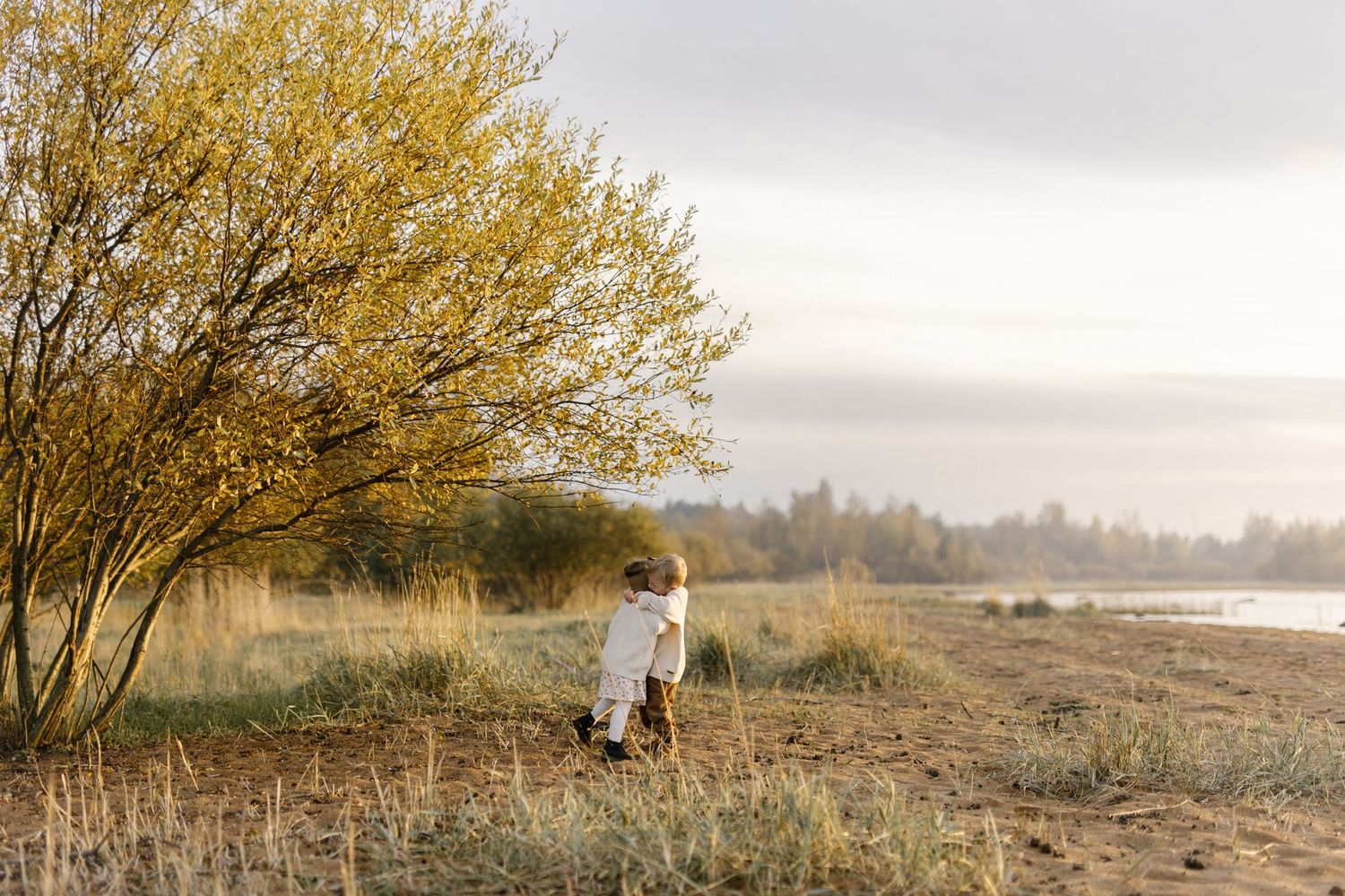 A solitary figure stands among autumn trees near a misty lake at sunset.