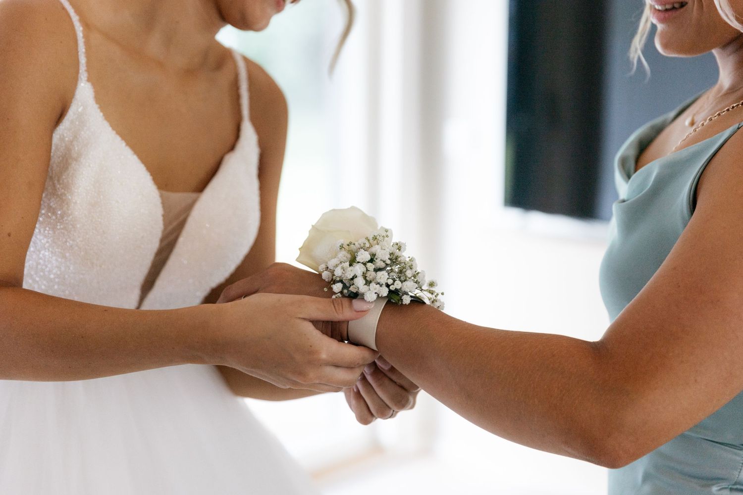 Close-up of delicate white wrist corsage being placed on bridesmaid.