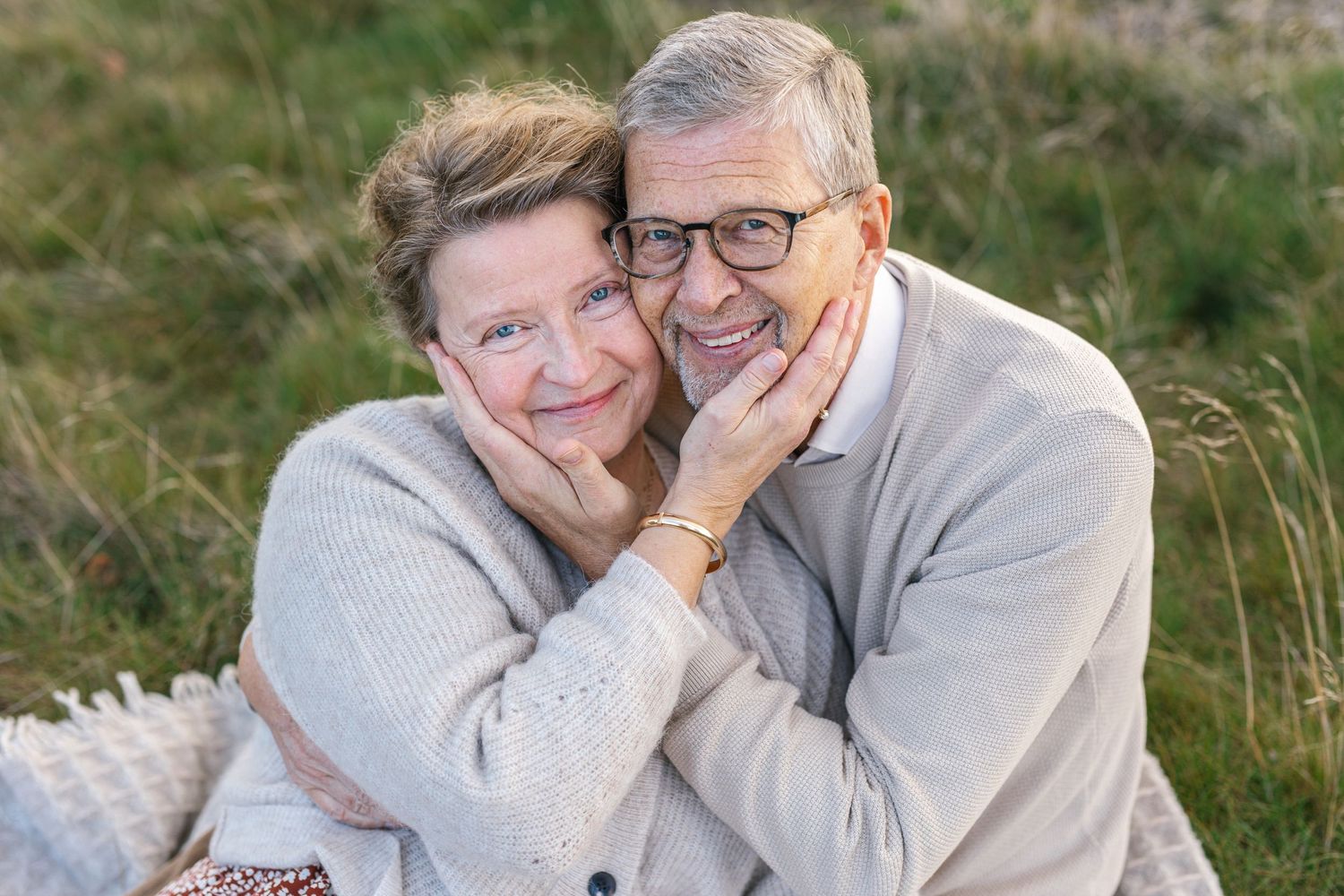 Senior couple in gray sweaters embrace while smiling outdoors.