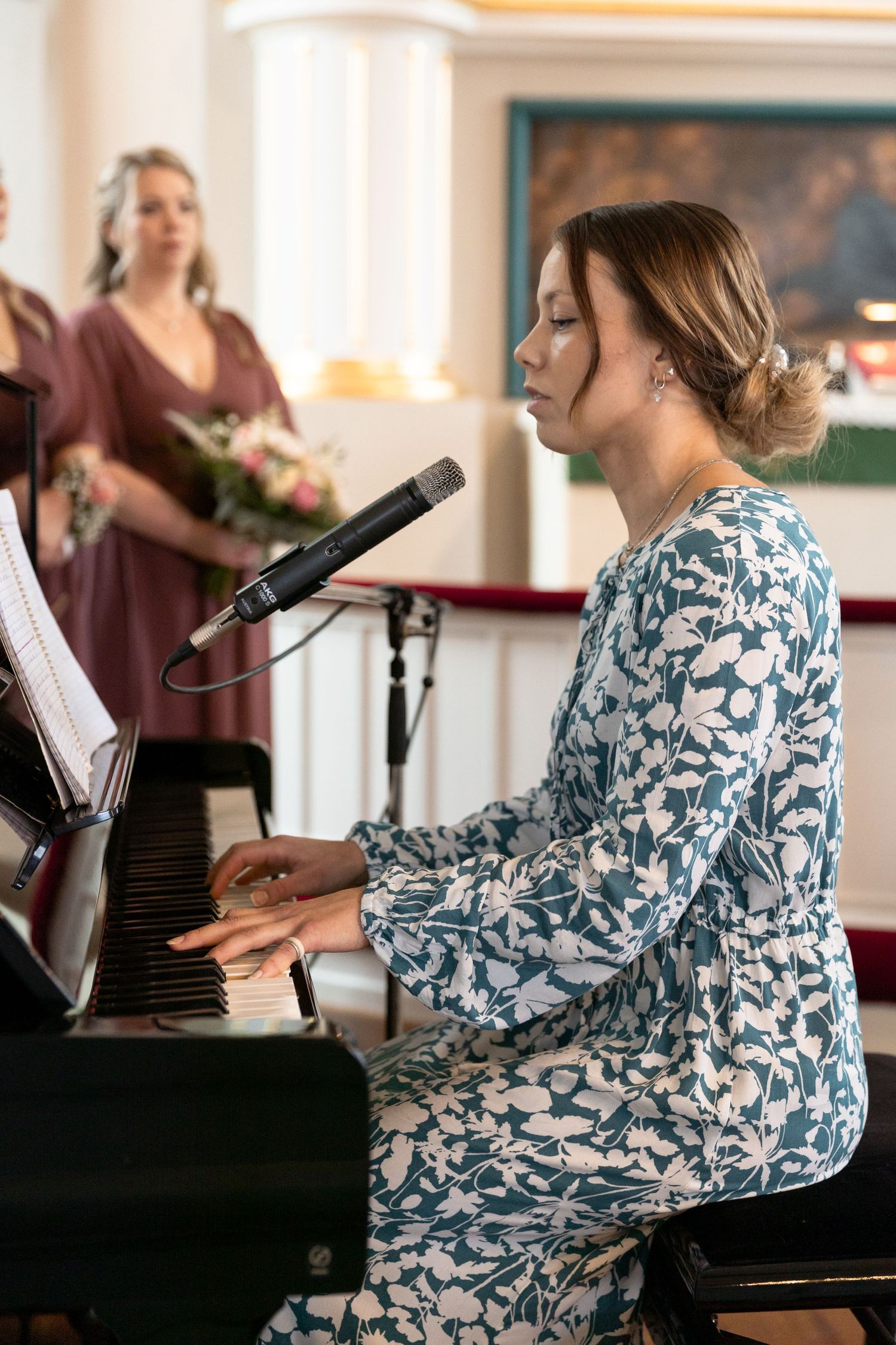 Musician in floral dress performs at piano during wedding celebration.