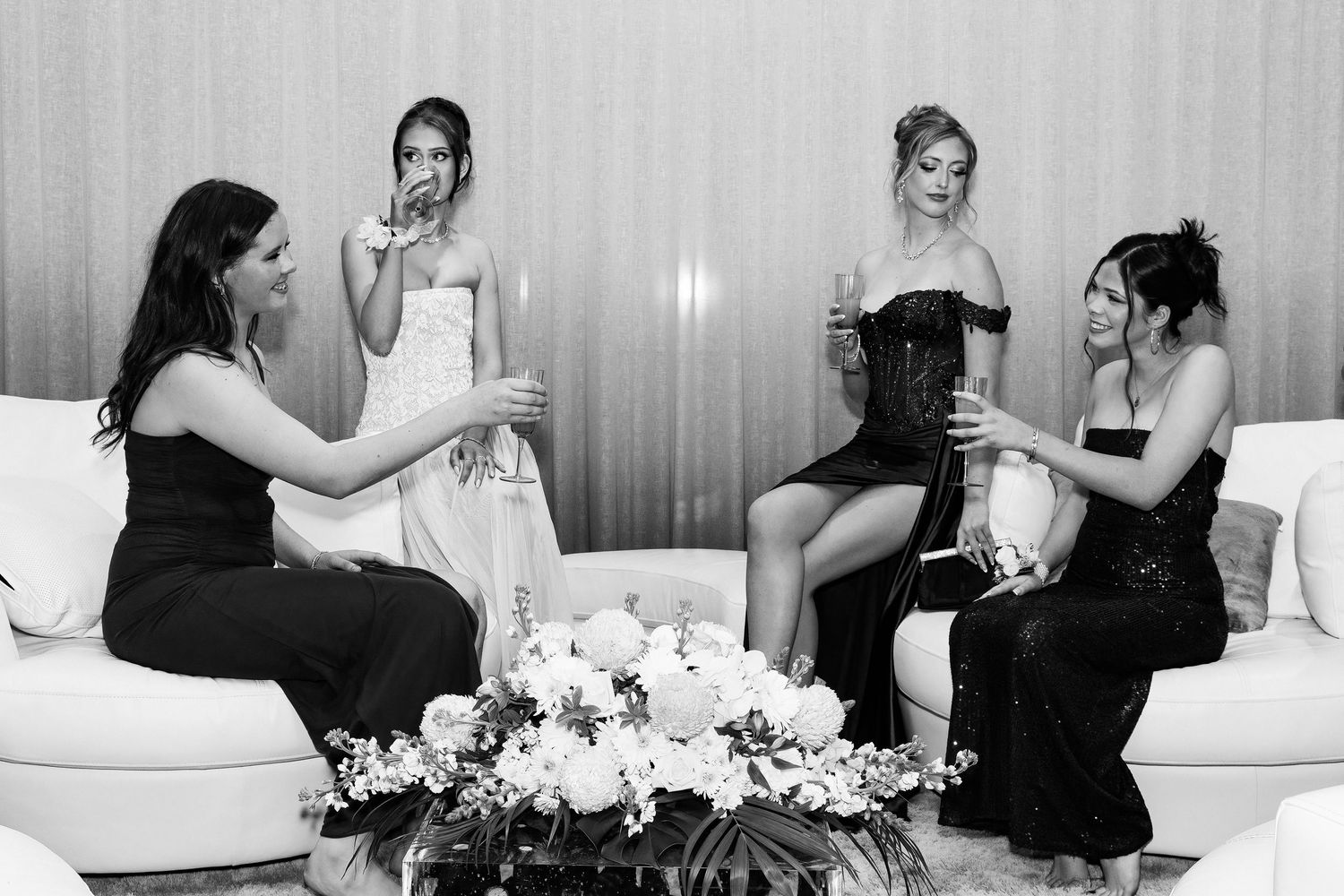 Four young women dressed for a pre-ball evening, with two raising glasses in a toast before the event