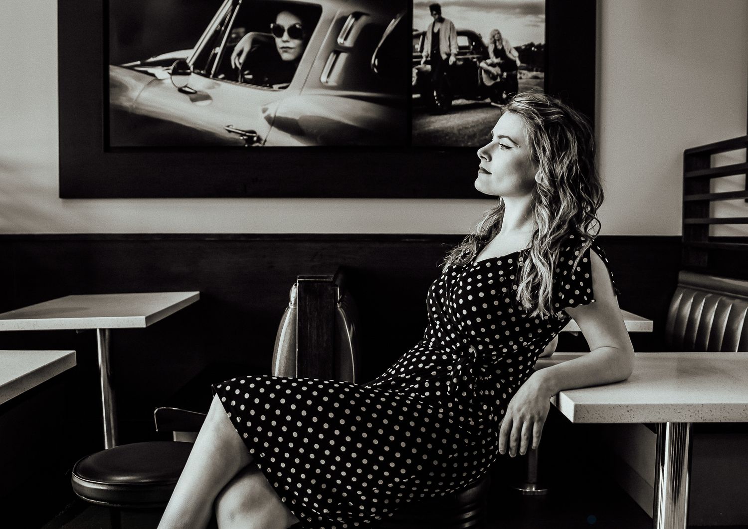 Black and white fashion portrait of a woman in a polka dot dress seated in a retro diner in Auckland