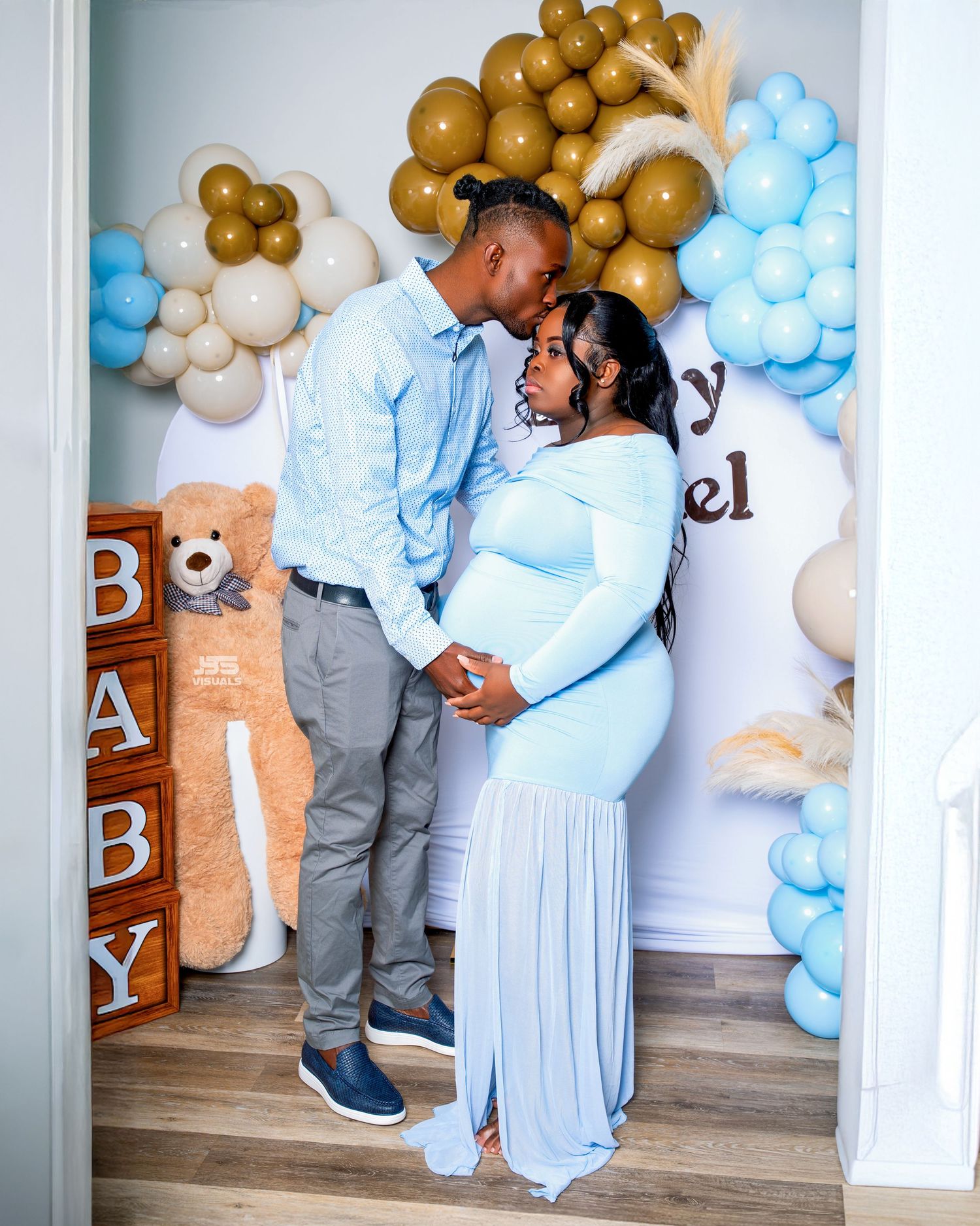 Couple shares a kiss at baby shower decorated with blue and gold balloons and teddy bears.