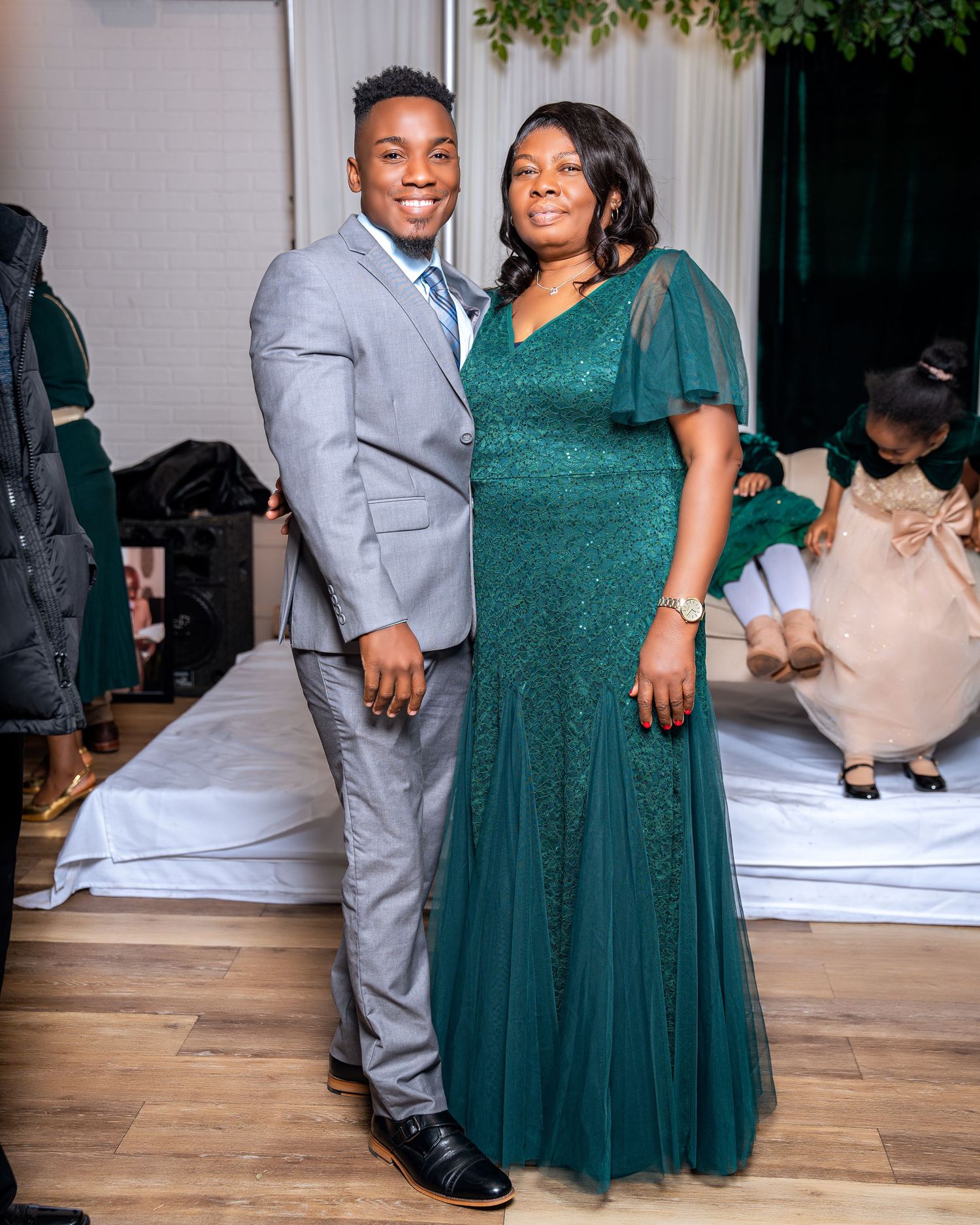 Young man in gray suit posing with woman in green gown at formal event.