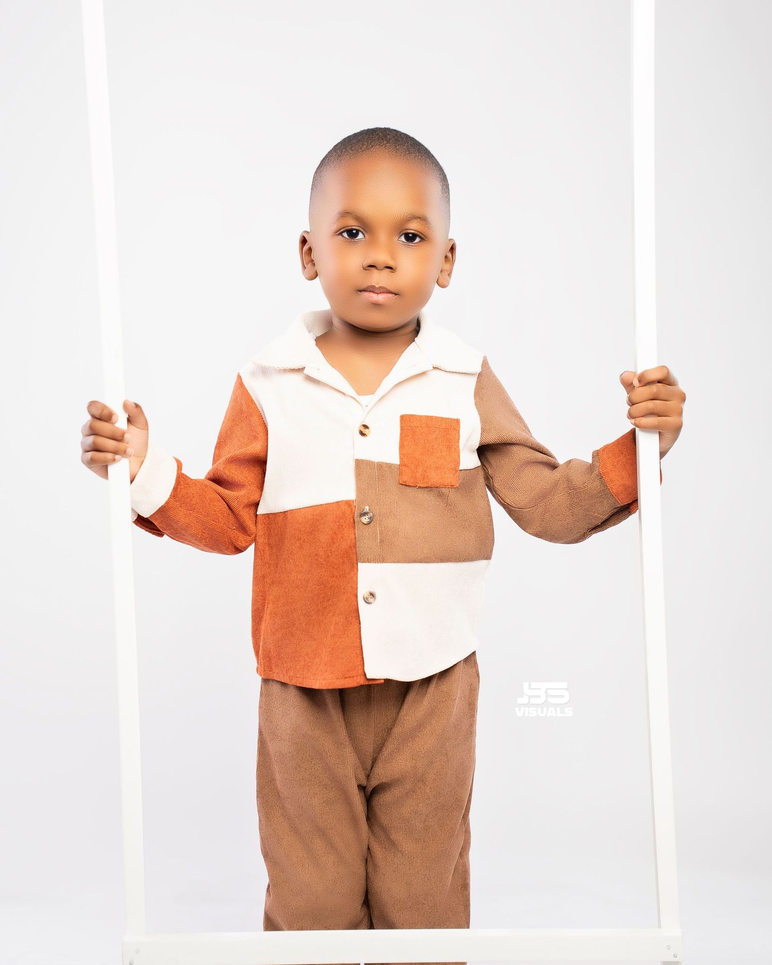 Young boy in colorblock corduroy shirt holding white swing frame against white background.