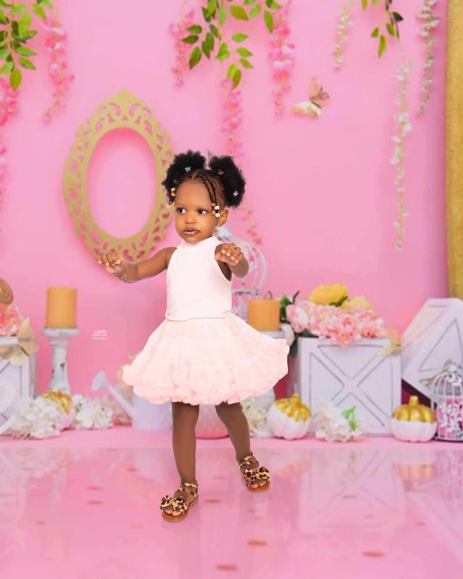 Adorable toddler girl in pink tutu dress and leopard sandals poses at a pink birthday photo shoot backdrop.