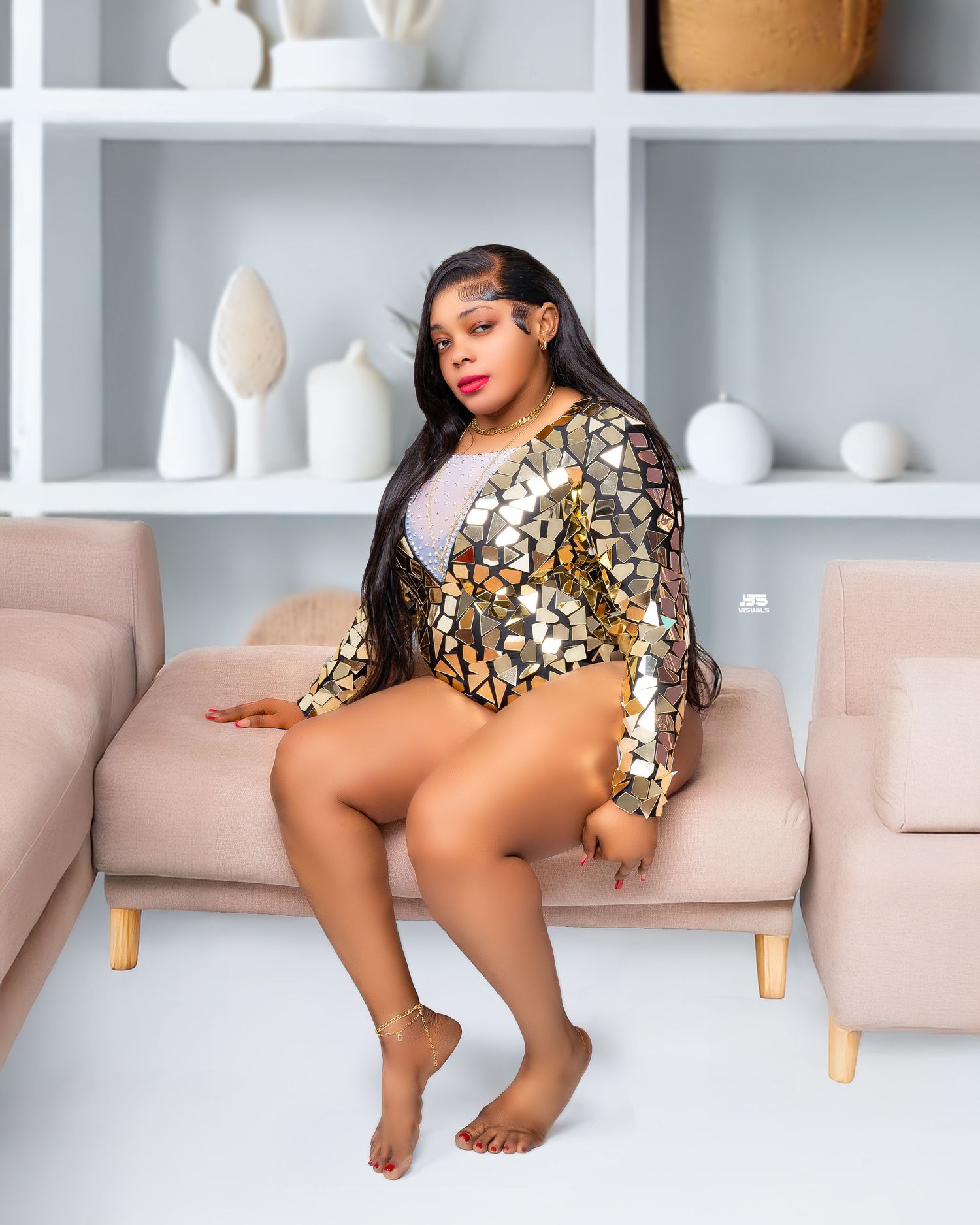 Woman in gold sequin bodysuit seated on beige sofa in bright modern living space.