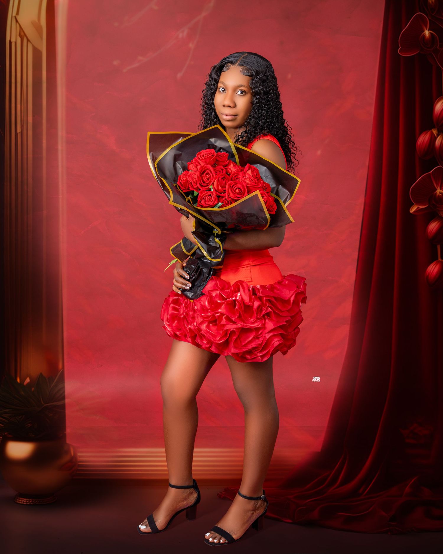 Young Black woman in red ruffled dress holds large rose bouquet in elegant red studio portrait.