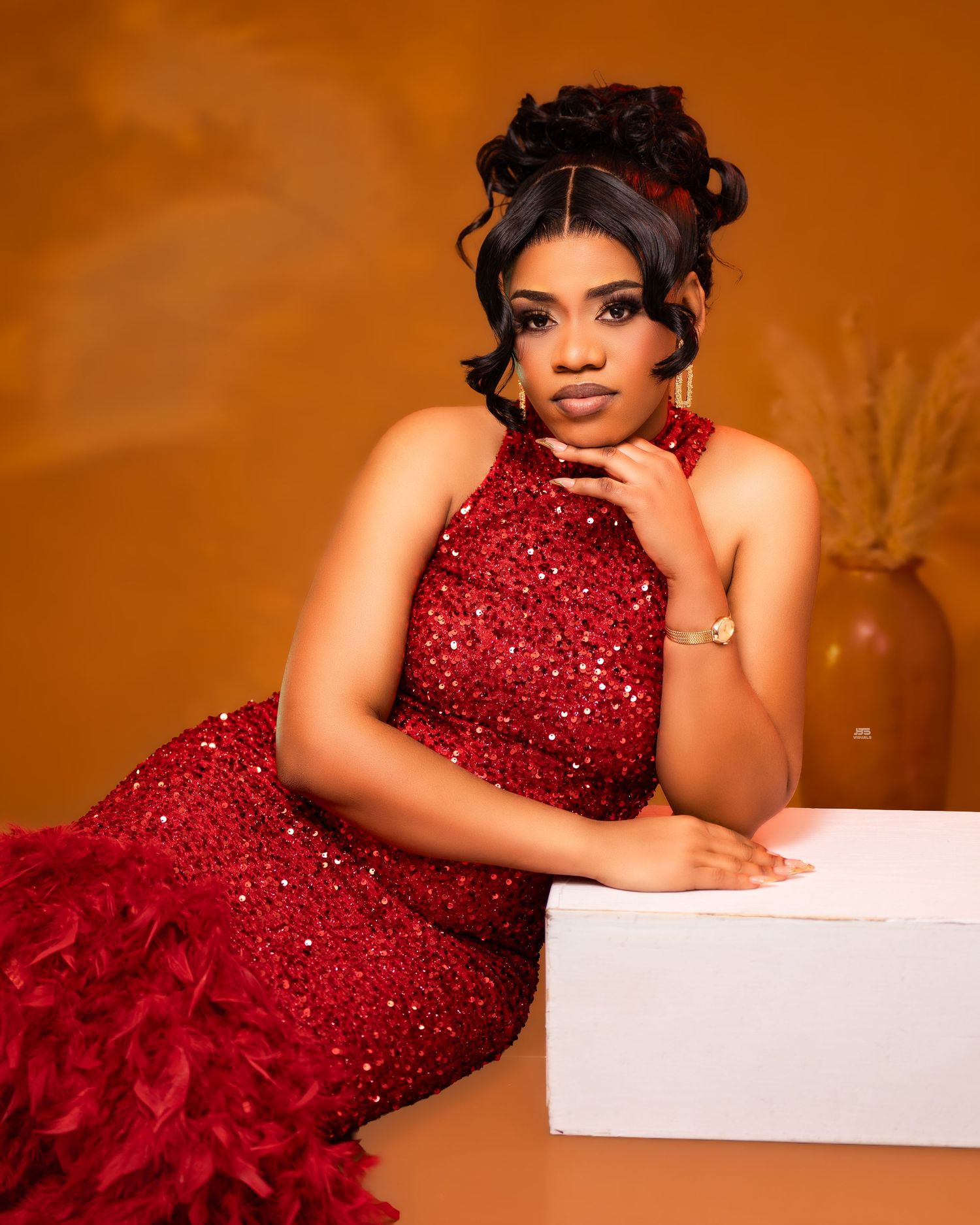 Woman in red sequined feather mermaid gown poses elegantly on white surface for birthday portrait.