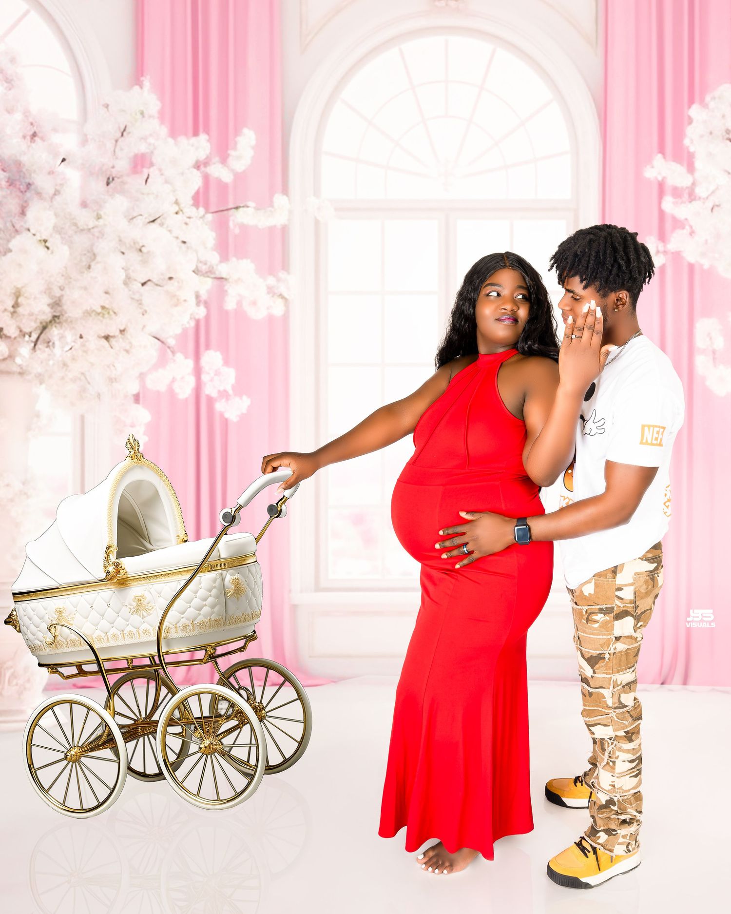 Pregnant woman in red dress with vintage pram poses with partner in pink floral maternity shoot.