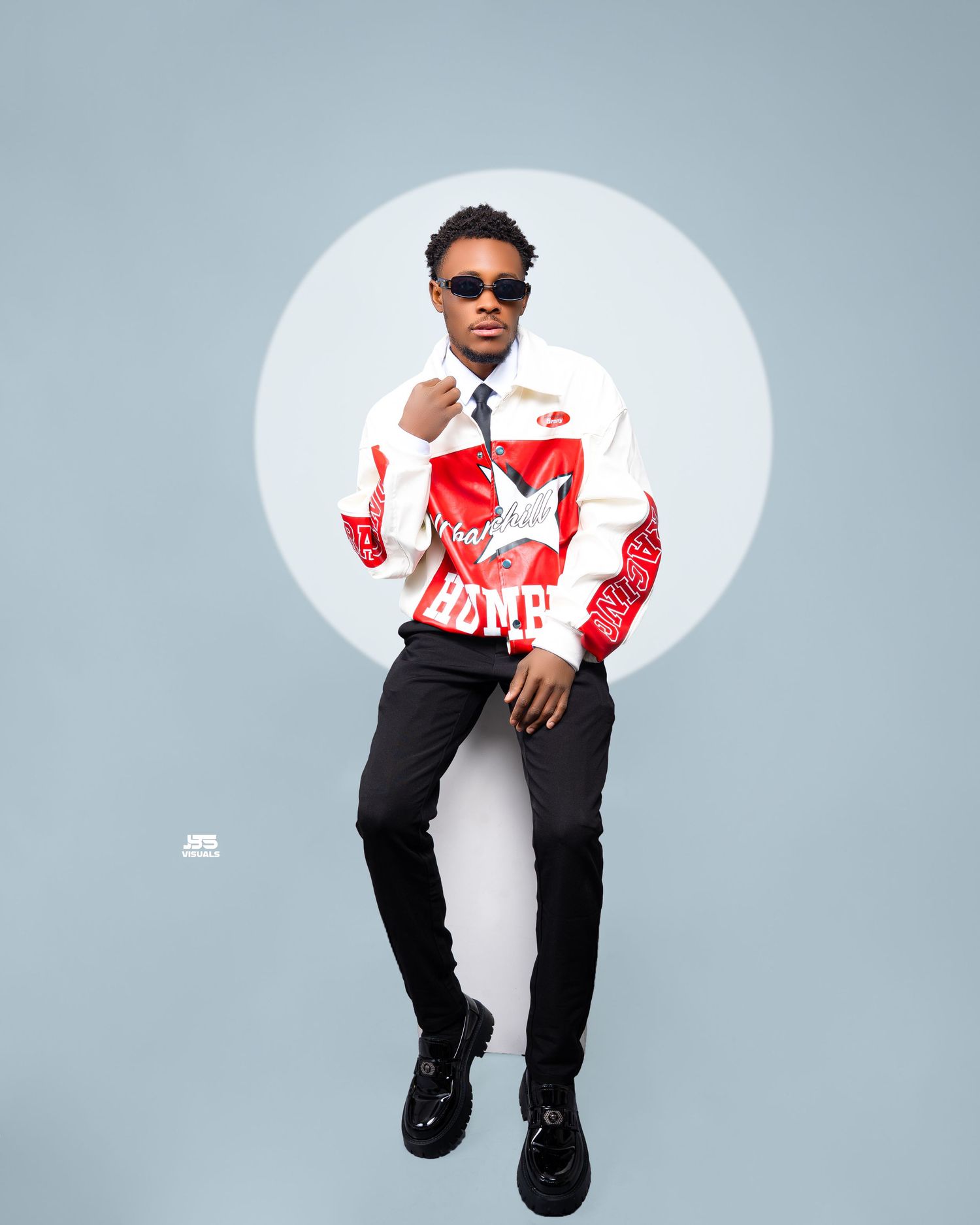 Stylish young man in red and white graphic jacket and sunglasses posing in studio.