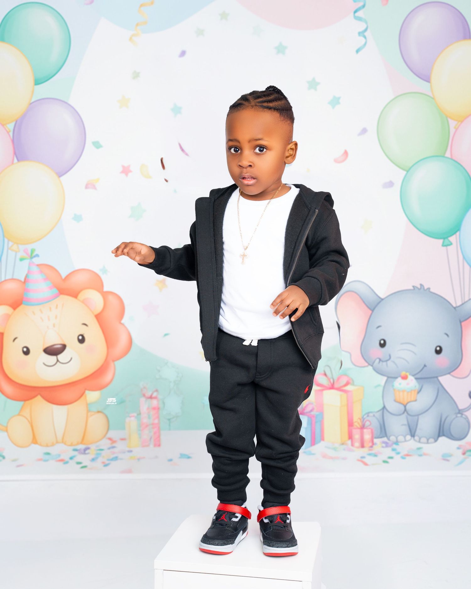 Young boy in black tracksuit and Jordan sneakers posing at a colorful birthday party backdrop.
