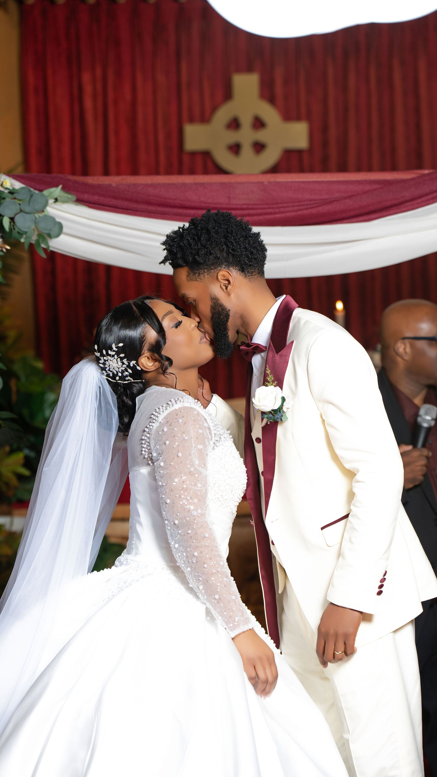 Bride and groom share their first kiss at the altar beneath a Celtic cross in a decorated church.