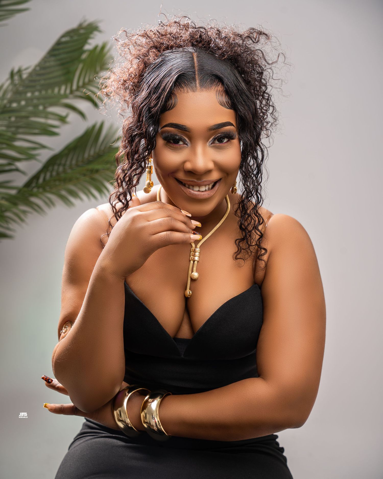 Woman in black dress with gold jewelry smiling confidently during a professional photo shoot.