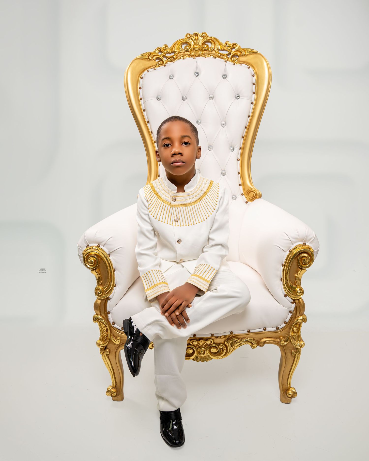 Young boy in elegant white and gold traditional outfit seated on a ornate gold throne chair.
