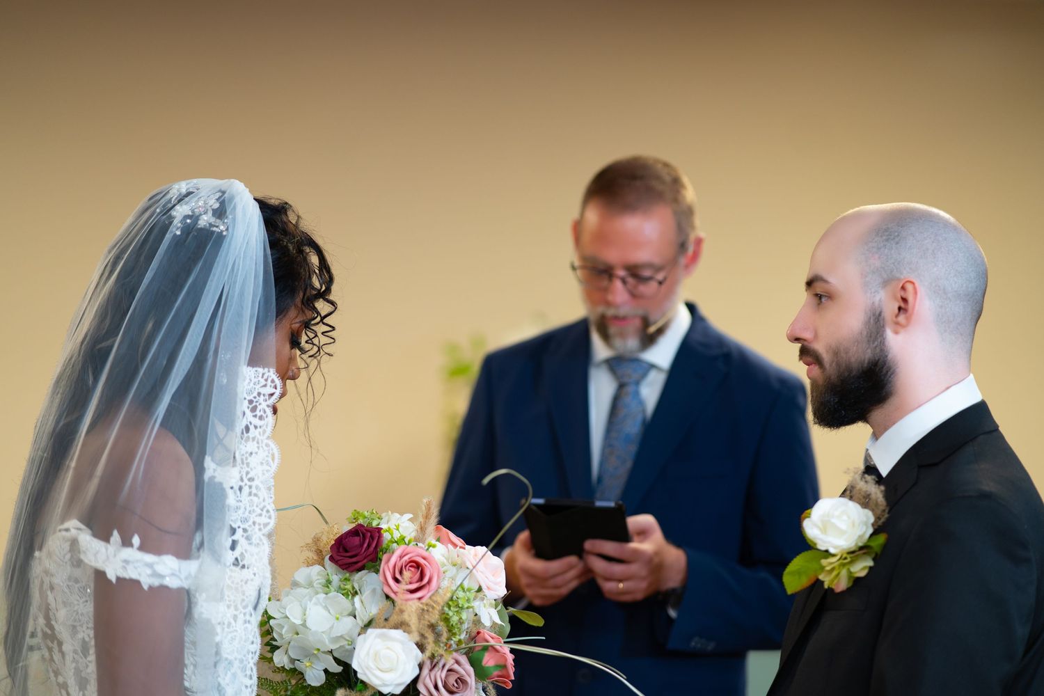 Bride and groom exchange vows before officiant in intimate wedding ceremony with floral bouquet.