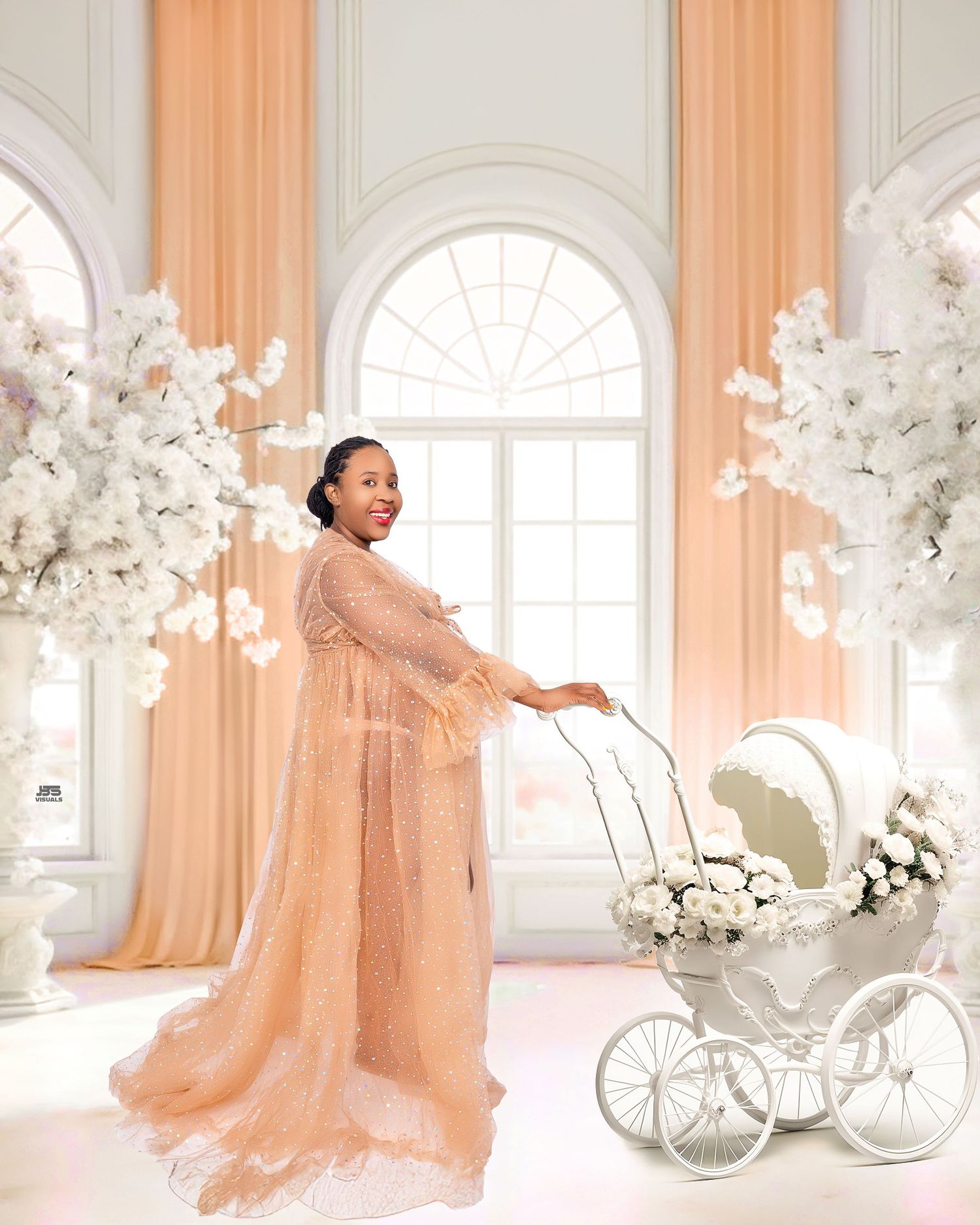 Elegant pregnant woman in champagne lace gown pushing a white floral baby carriage in studio.