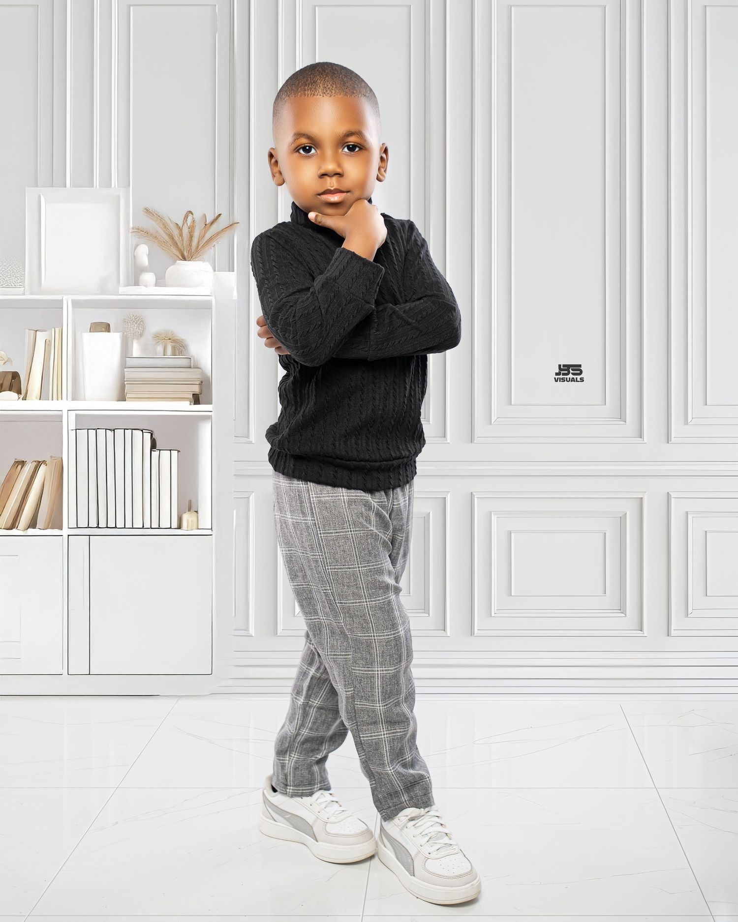 Young boy in black sweater and plaid pants posing thoughtfully in white modern interior.