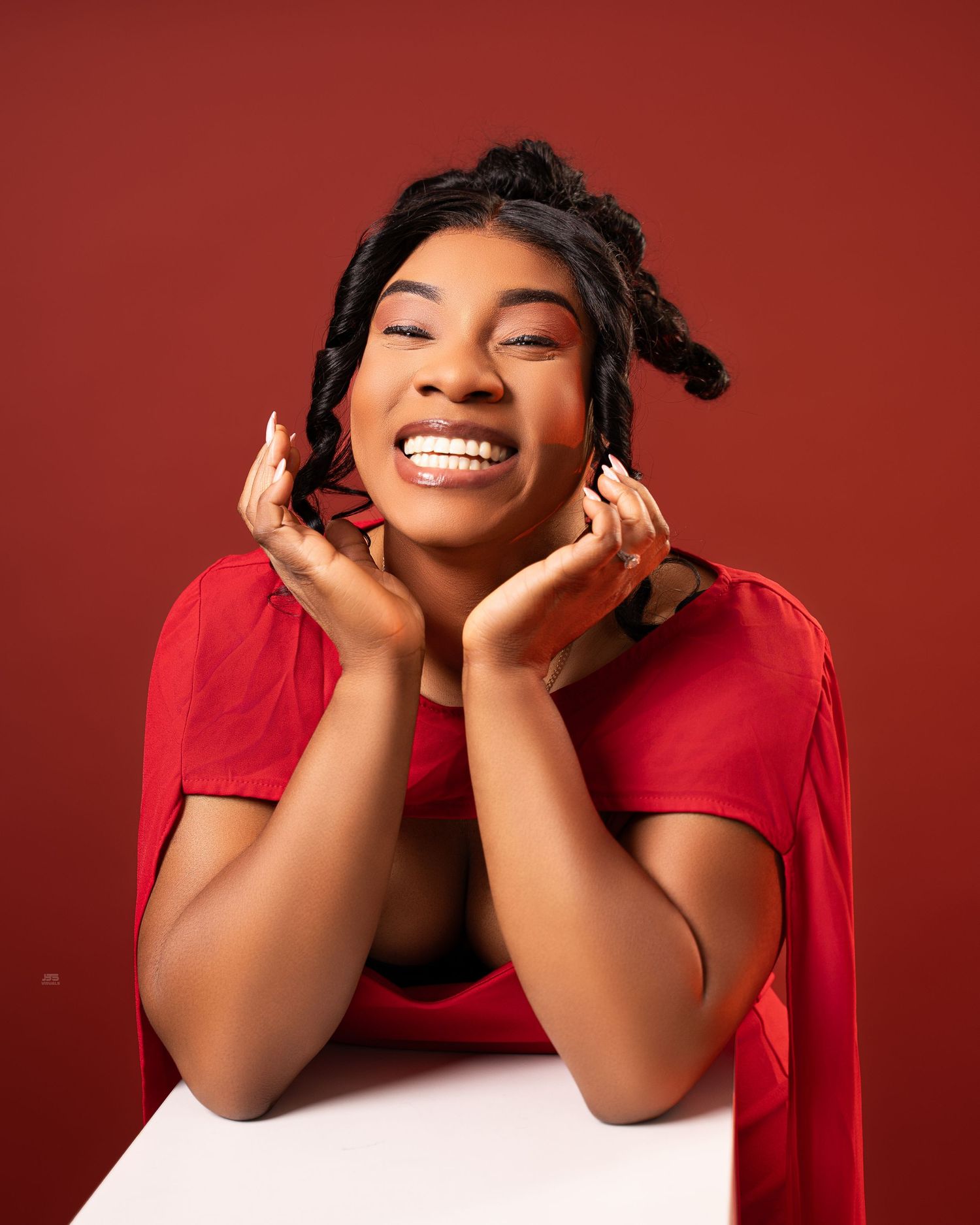 Joyful woman in red outfit laughing with hands on cheeks against red background.