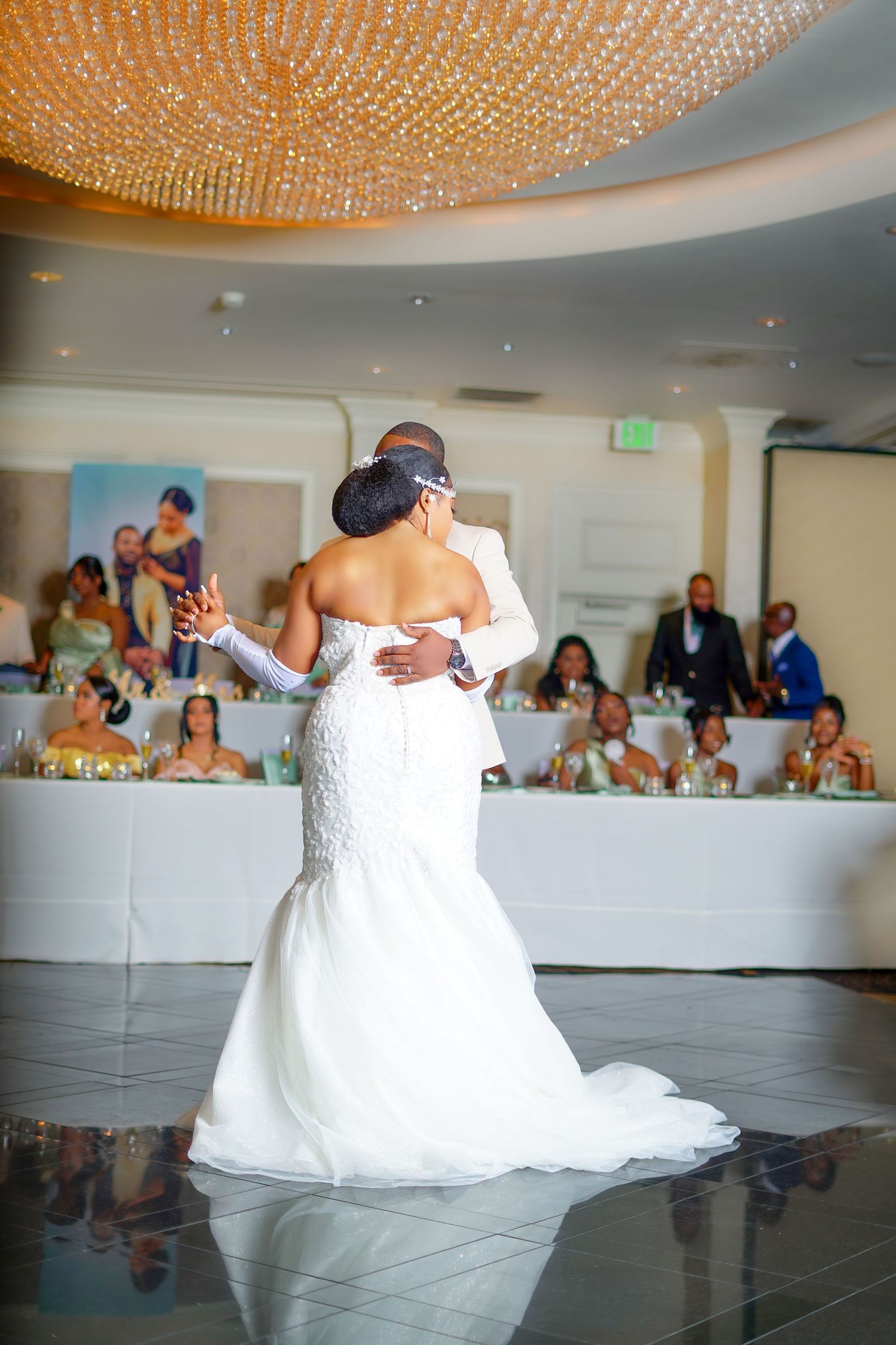Bride and groom share romantic first dance under crystal chandelier at elegant wedding reception.