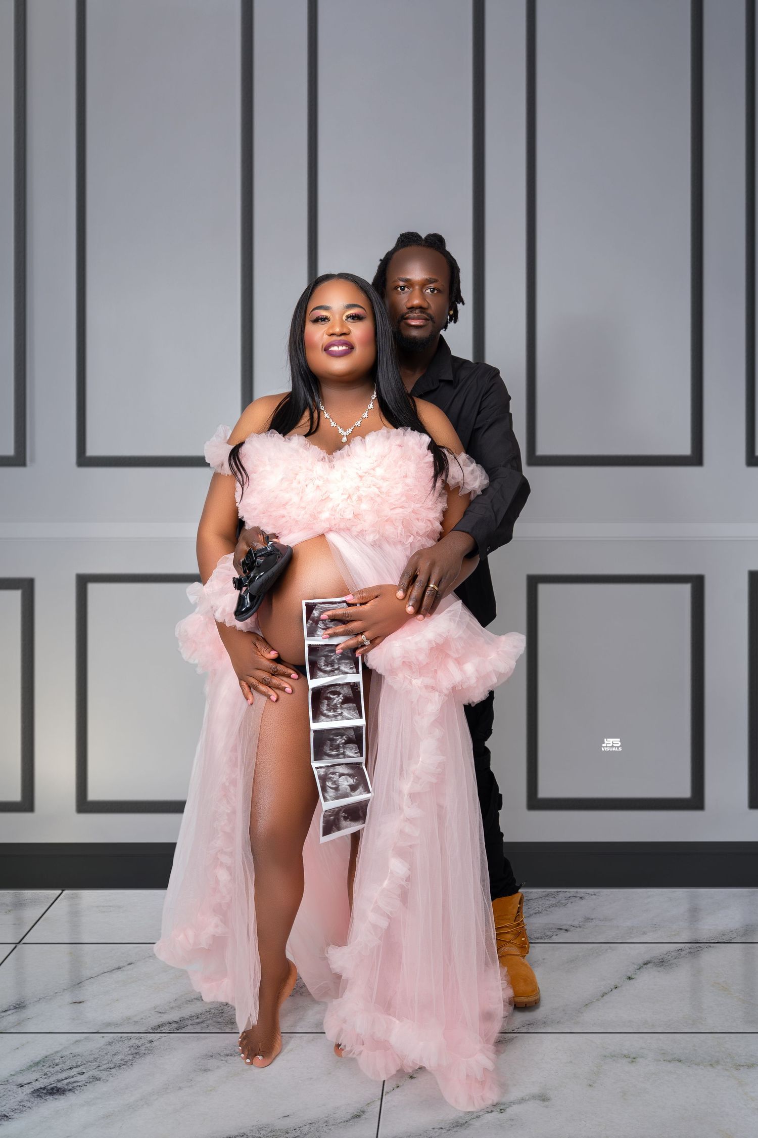 Expecting couple in studio holding ultrasound photos, woman in pink tulle maternity gown.