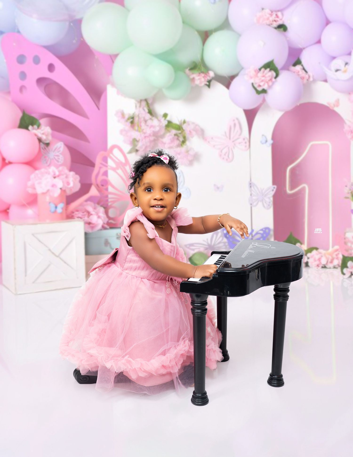 Baby girl in pink tutu dress playing toy piano at butterfly-themed first birthday photo shoot.