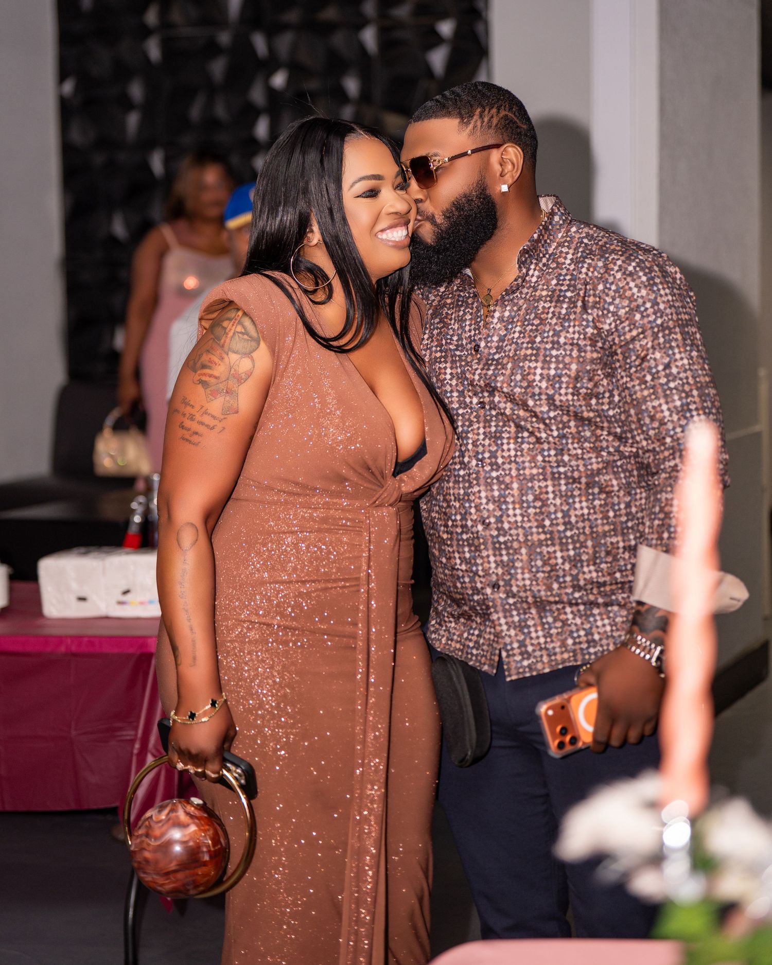 Couple in brown outfits sharing a kiss at a festive indoor party event.