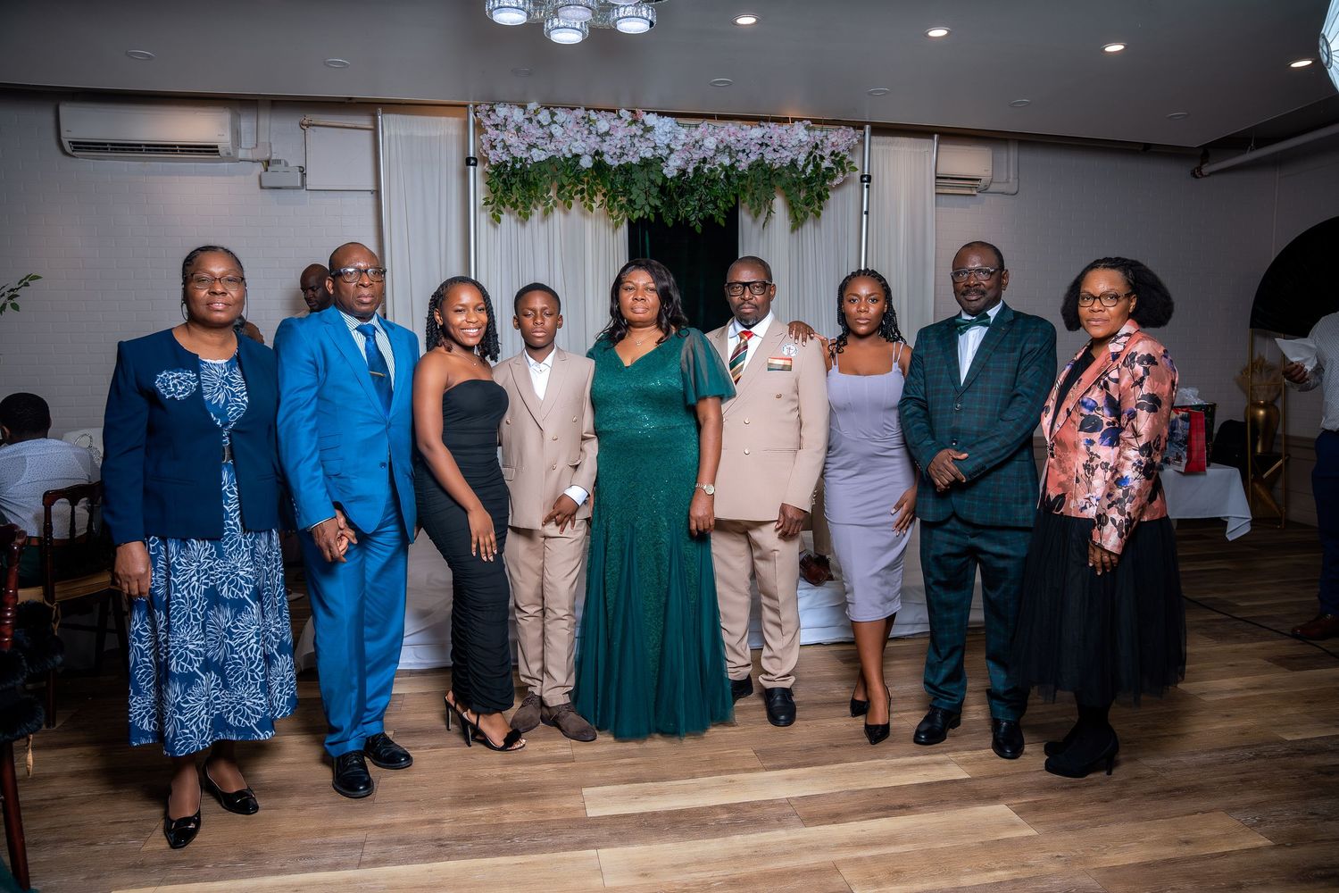 Group of eight formally dressed people posing together at an elegant indoor event.