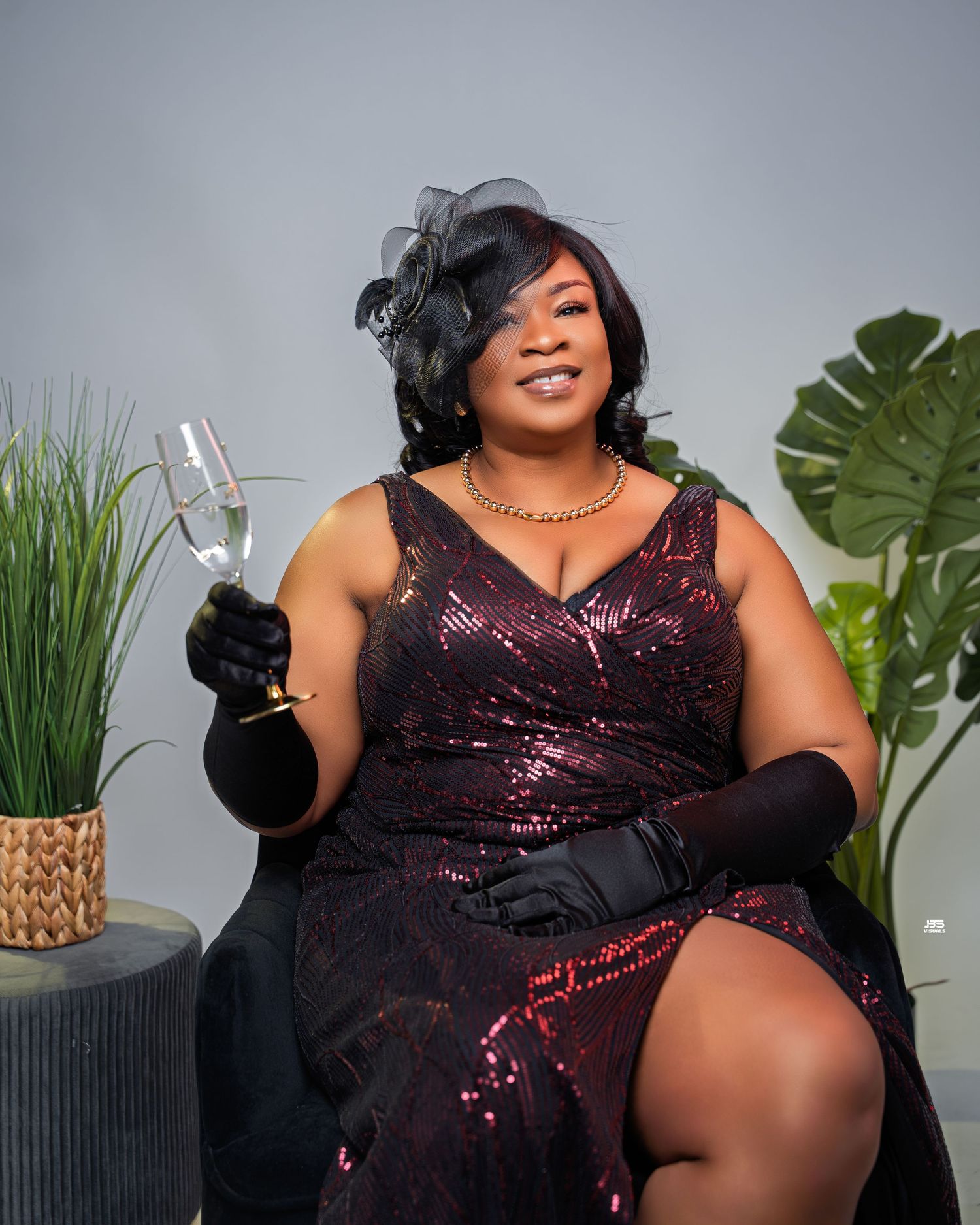 Glamorous woman in sequined burgundy dress holds a champagne glass in an elegant studio setting.