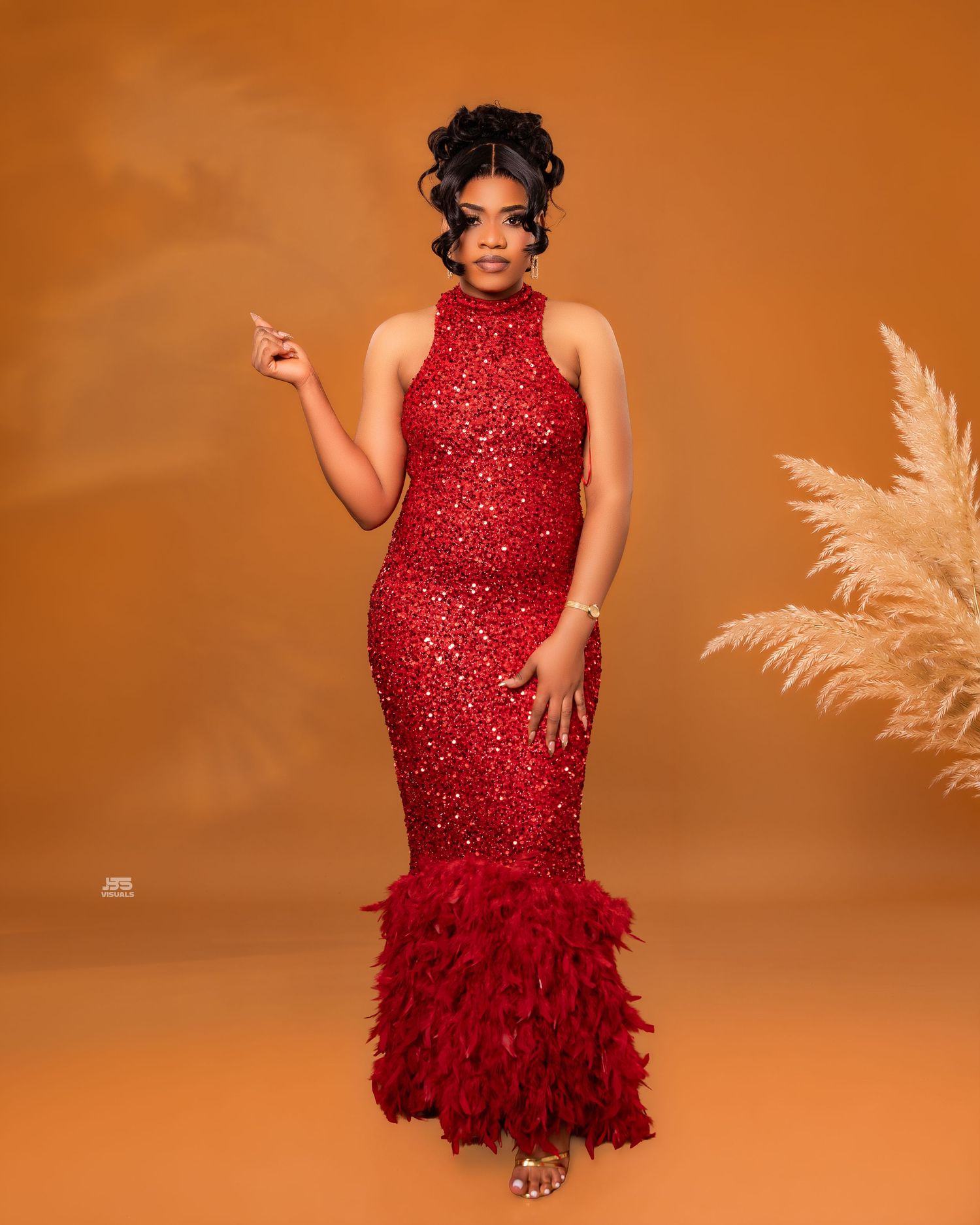 Woman in red sequined feather mermaid gown poses confidently in warm-toned studio with pampas grass.