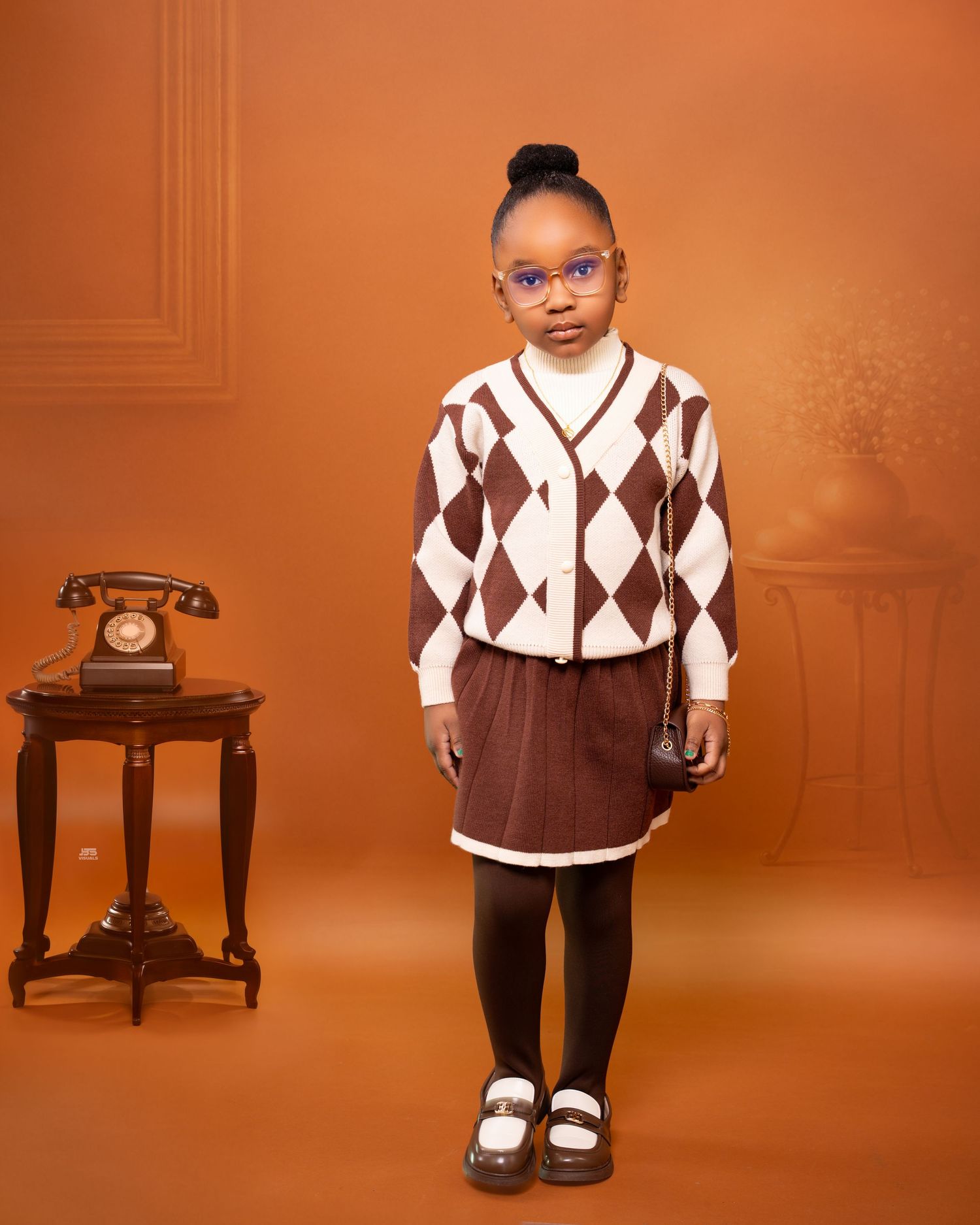 Young girl in brown argyle cardigan and skirt standing in vintage-styled photography studio.