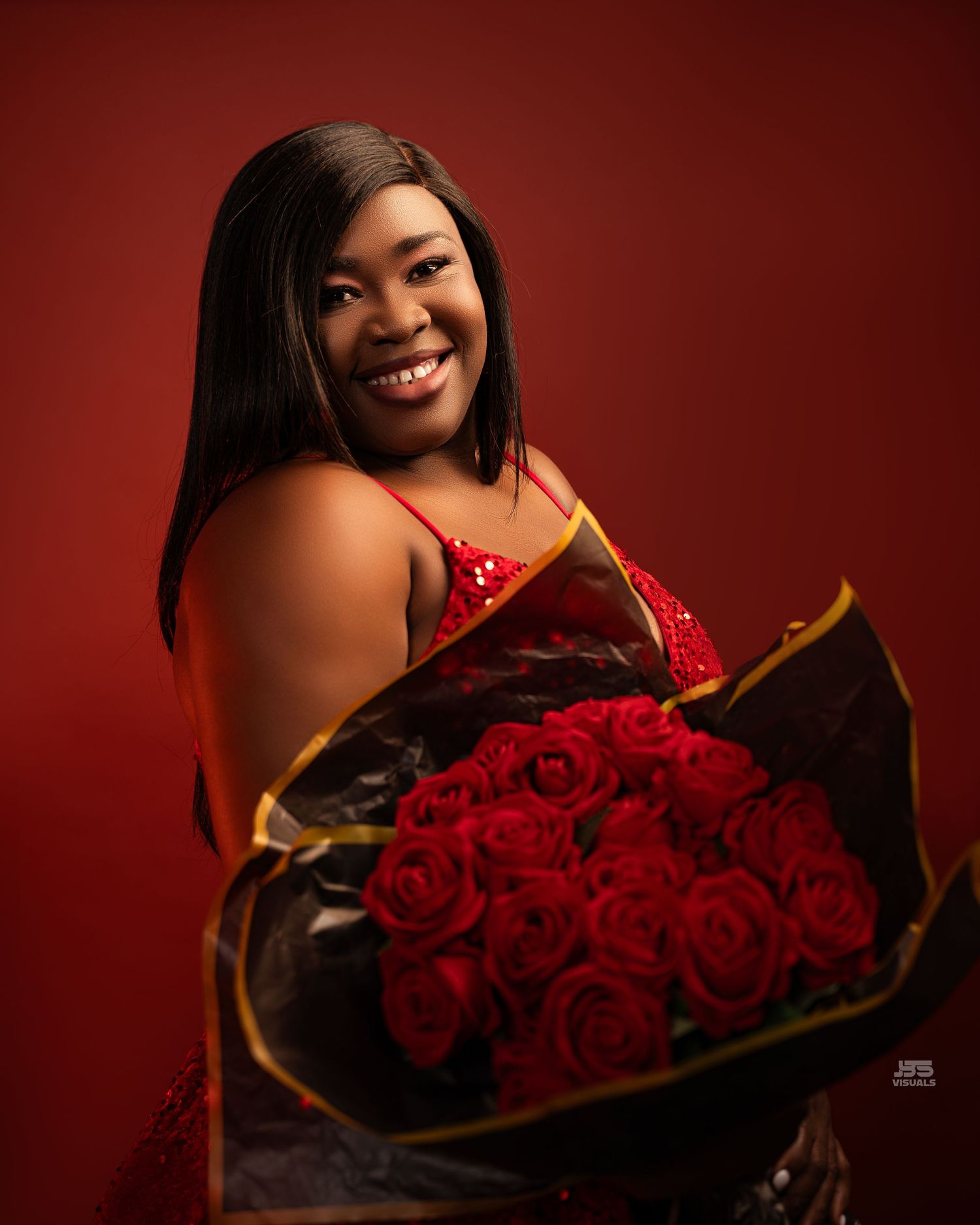 Smiling woman in red sequin dress holding bouquet of red roses against red background.
