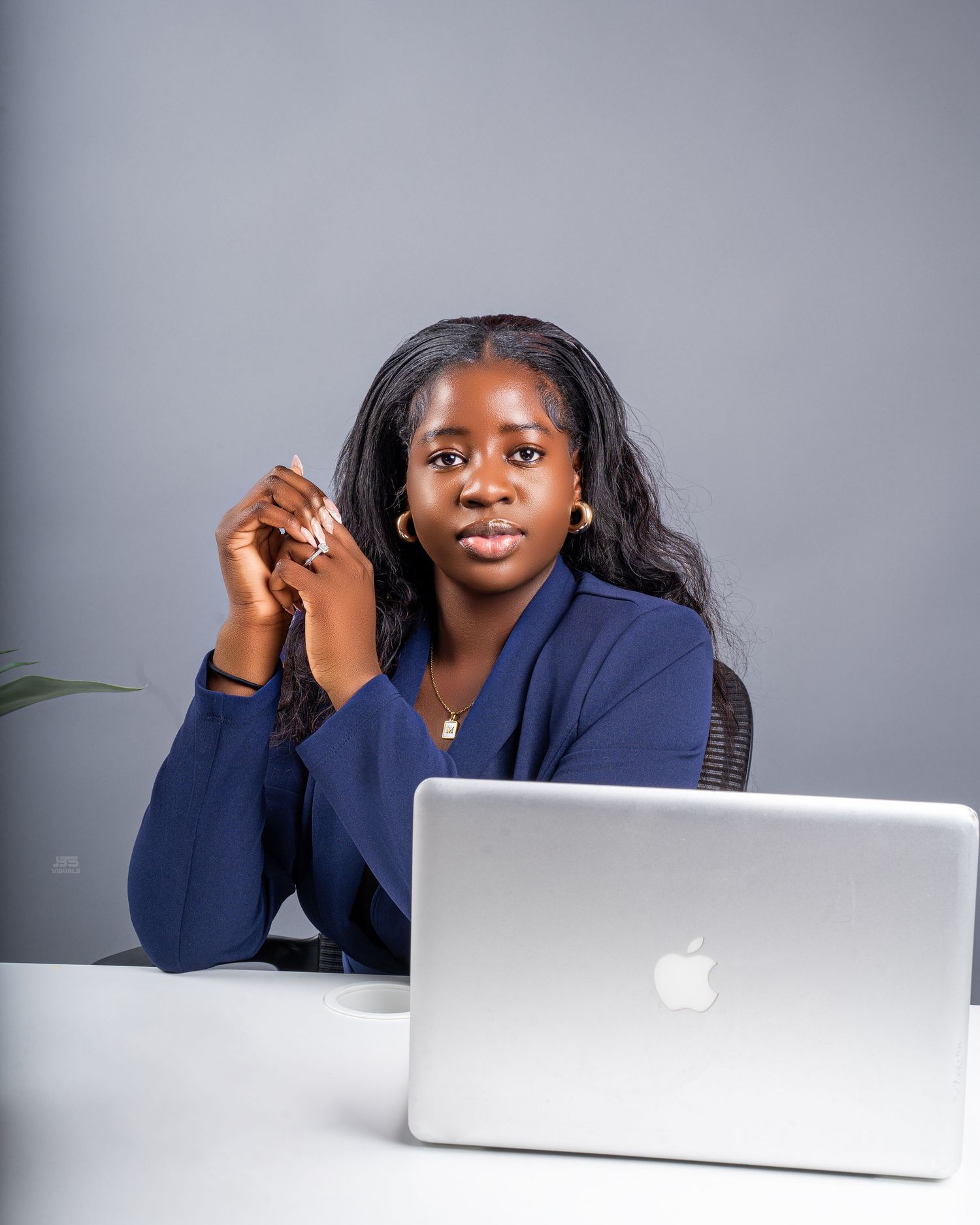 Professional woman in navy blazer sitting at desk with Apple MacBook laptop in gray studio.