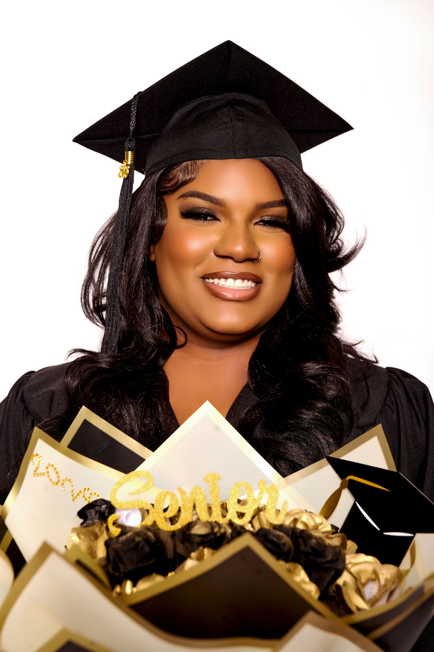Smiling graduate in black cap and gown holding a gold and black Senior bouquet arrangement.