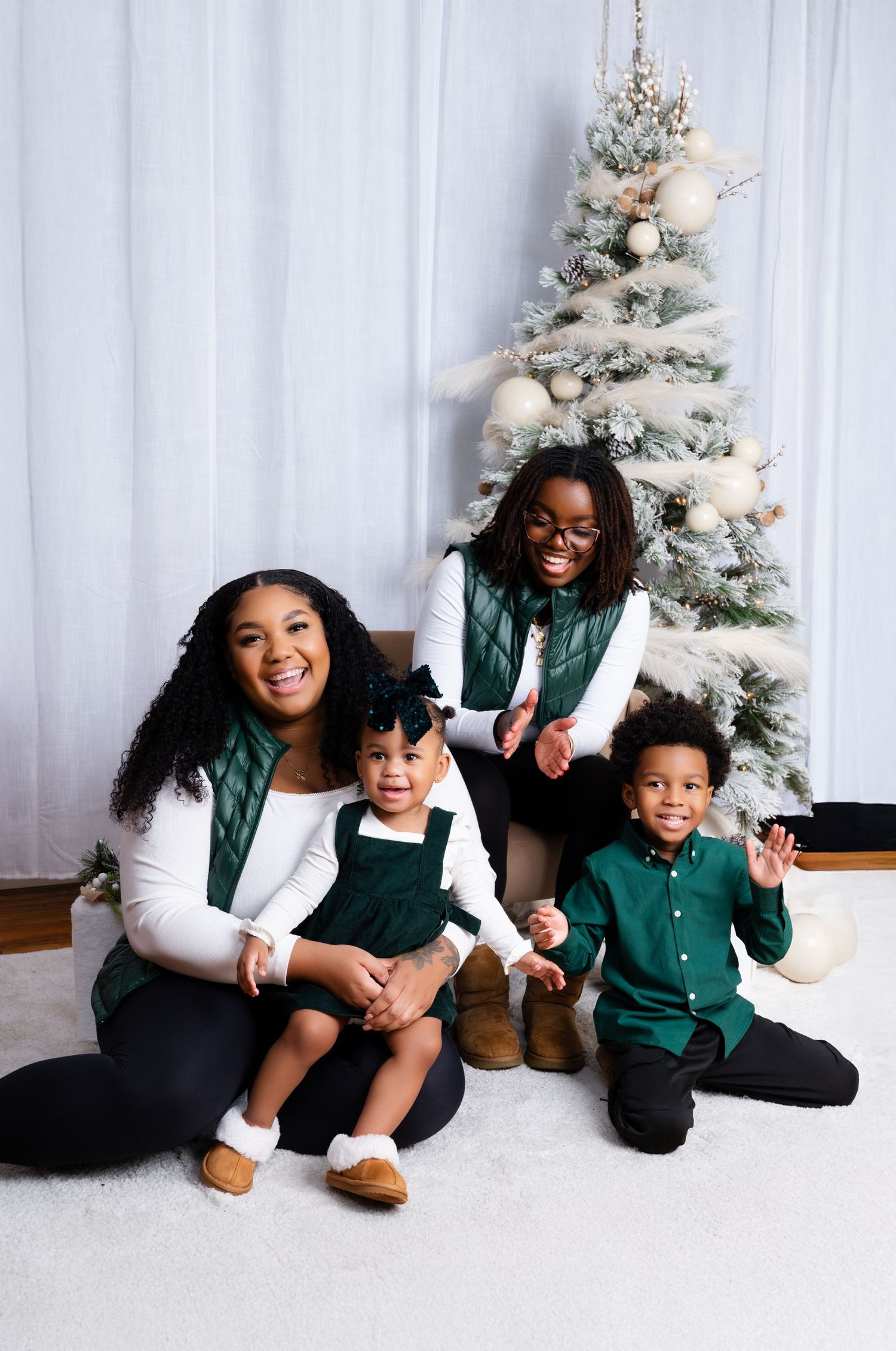 Family of four in matching green outfits posing together near a decorated Christmas tree for a holiday portrait.