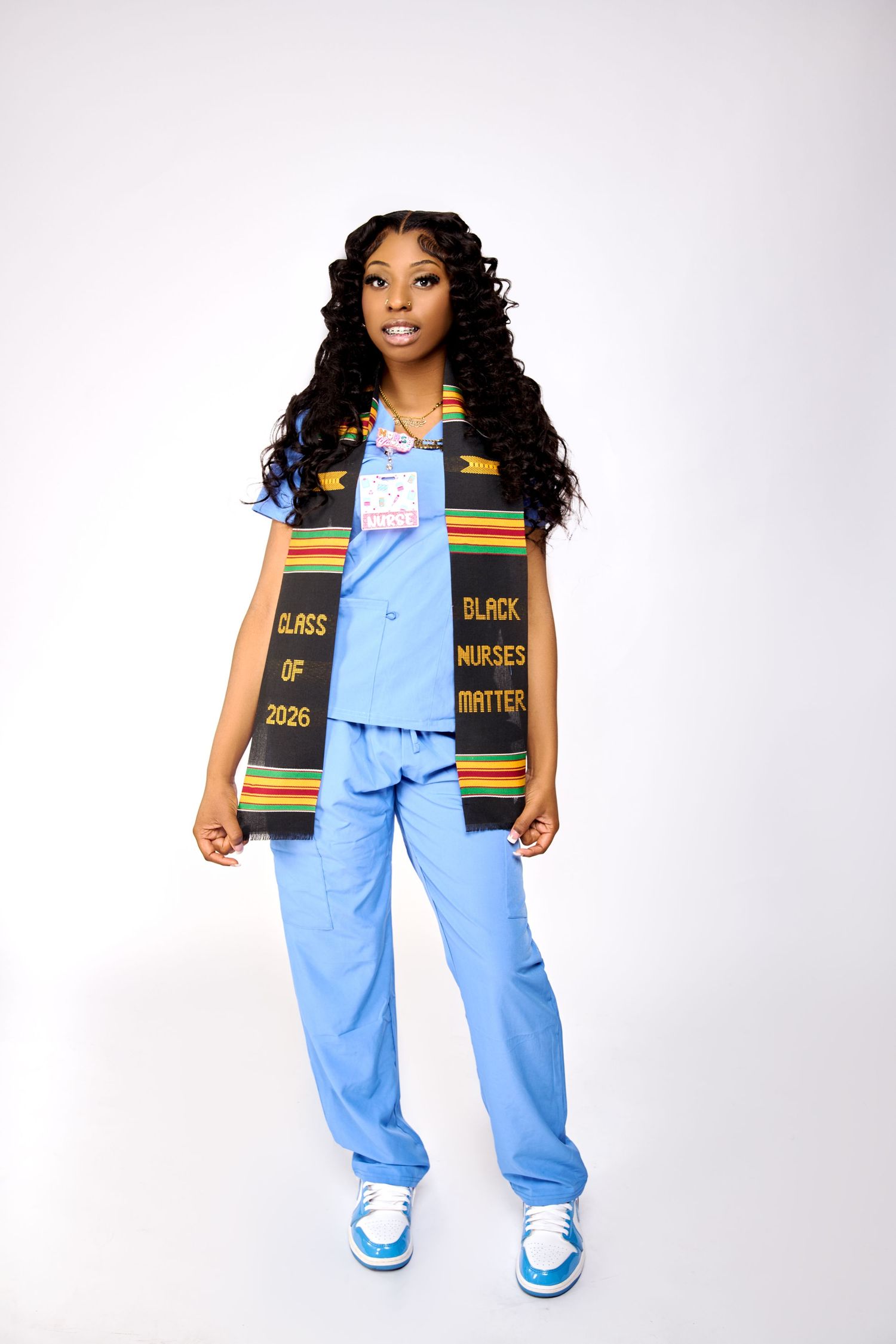 Nursing student in blue scrubs wearing a Black Nurses Matter kente stole, Class of 2026, posing confidently.
