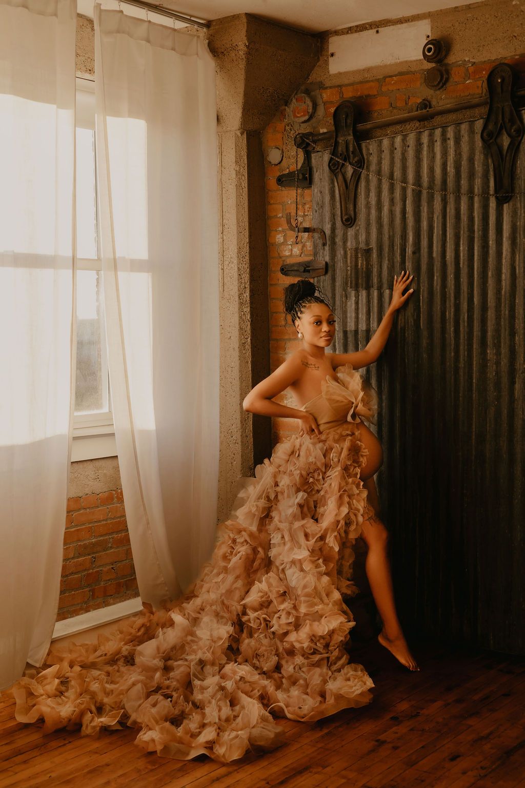 A dancer in a flowing beige ruffled dress performs dramatic movements in a rustic room with wooden floors and walls.