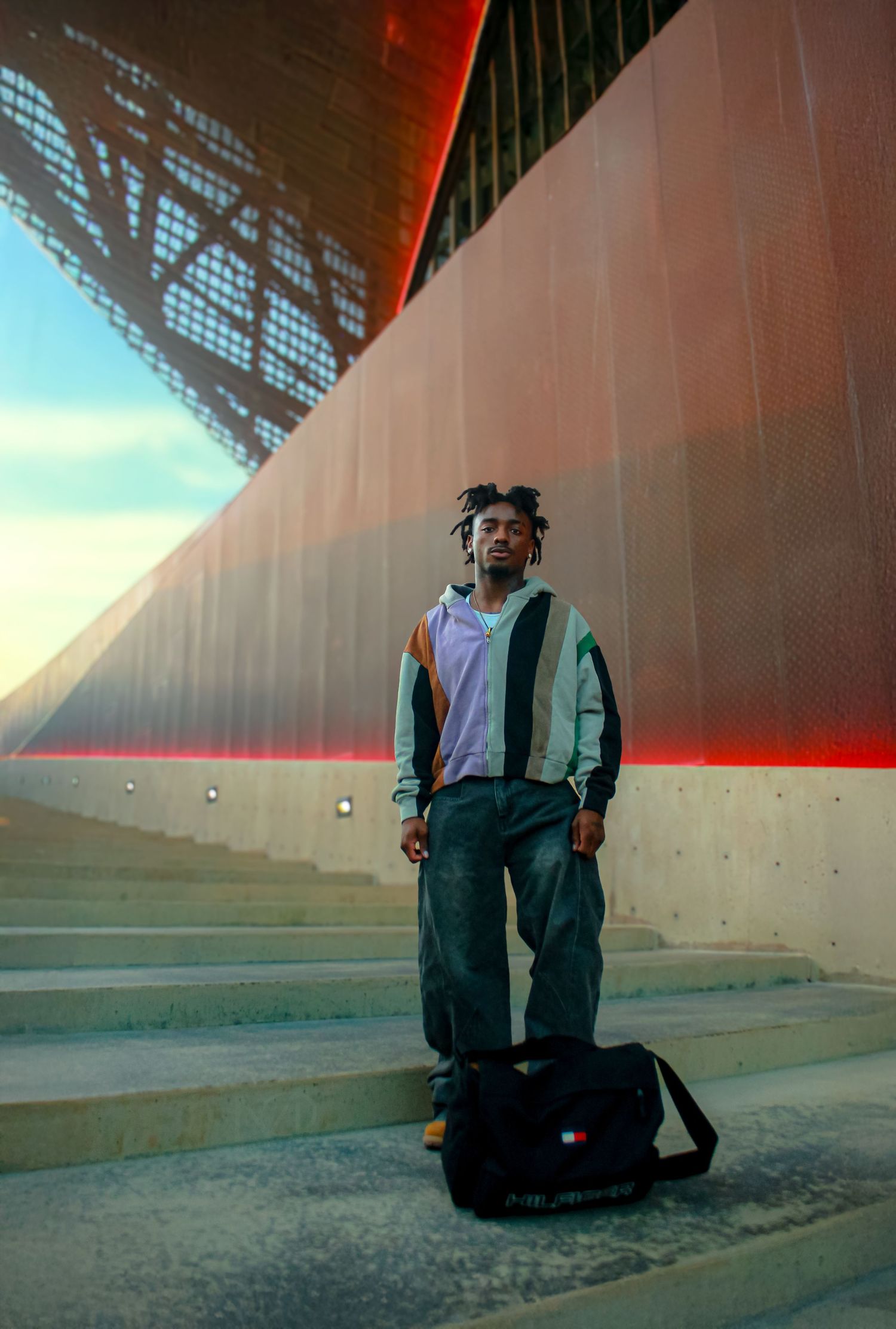 Person in casual attire sits on concrete steps during golden hour with dramatic shadows.