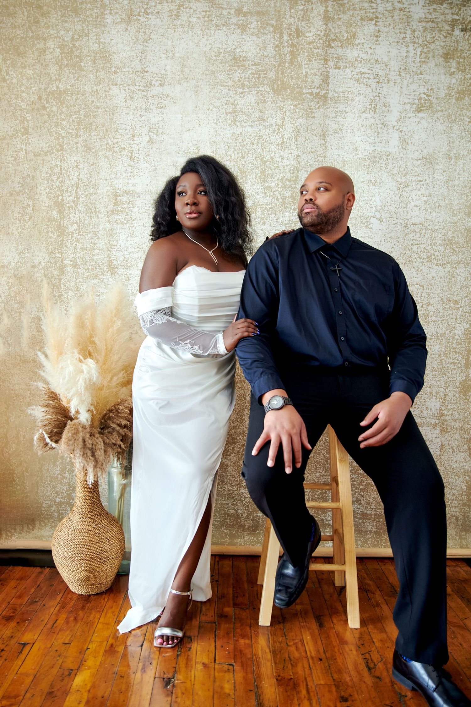 A couple sits together on wooden chairs against a textured wall in a creative photo series.