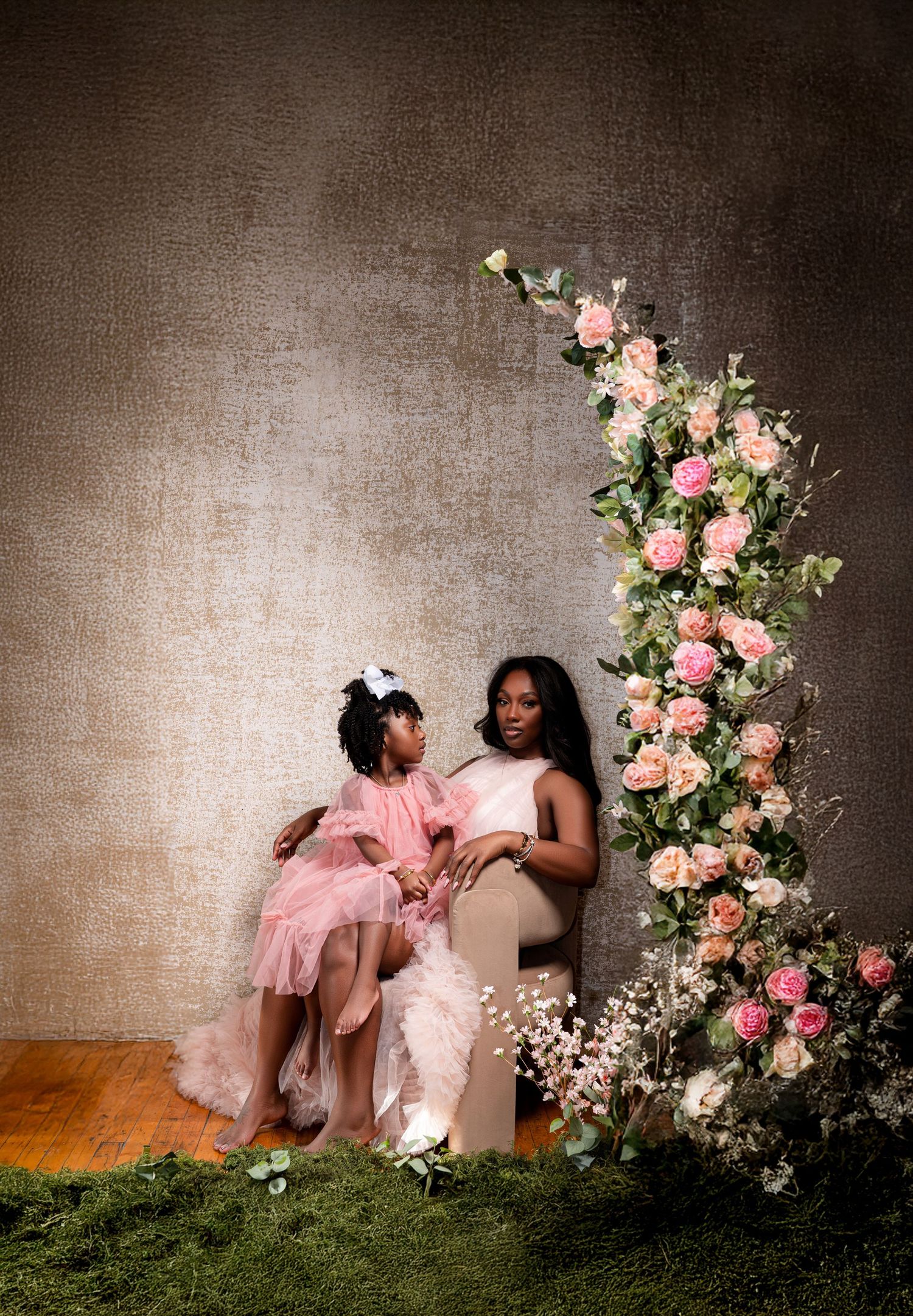 Romantic portrait session with pink floral arrangements against textured gray backdrop.