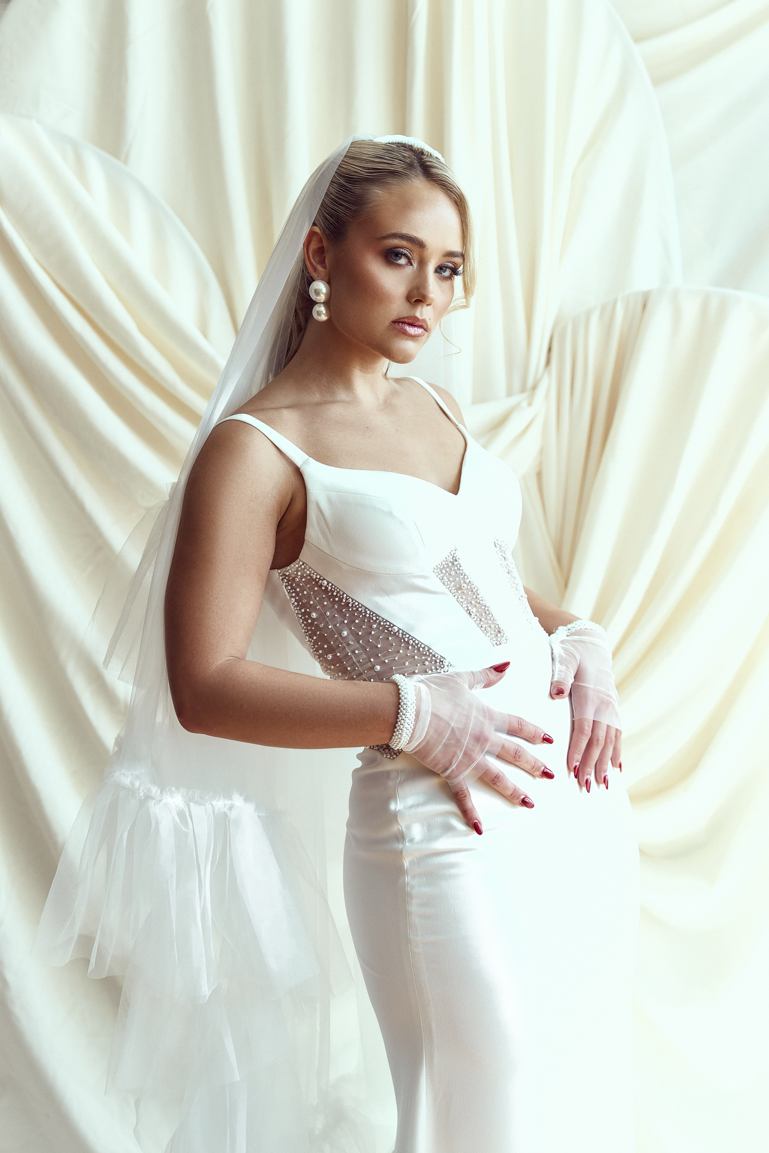 A bride in a white wedding dress poses elegantly against a draped ivory fabric backdrop in a series of photos.