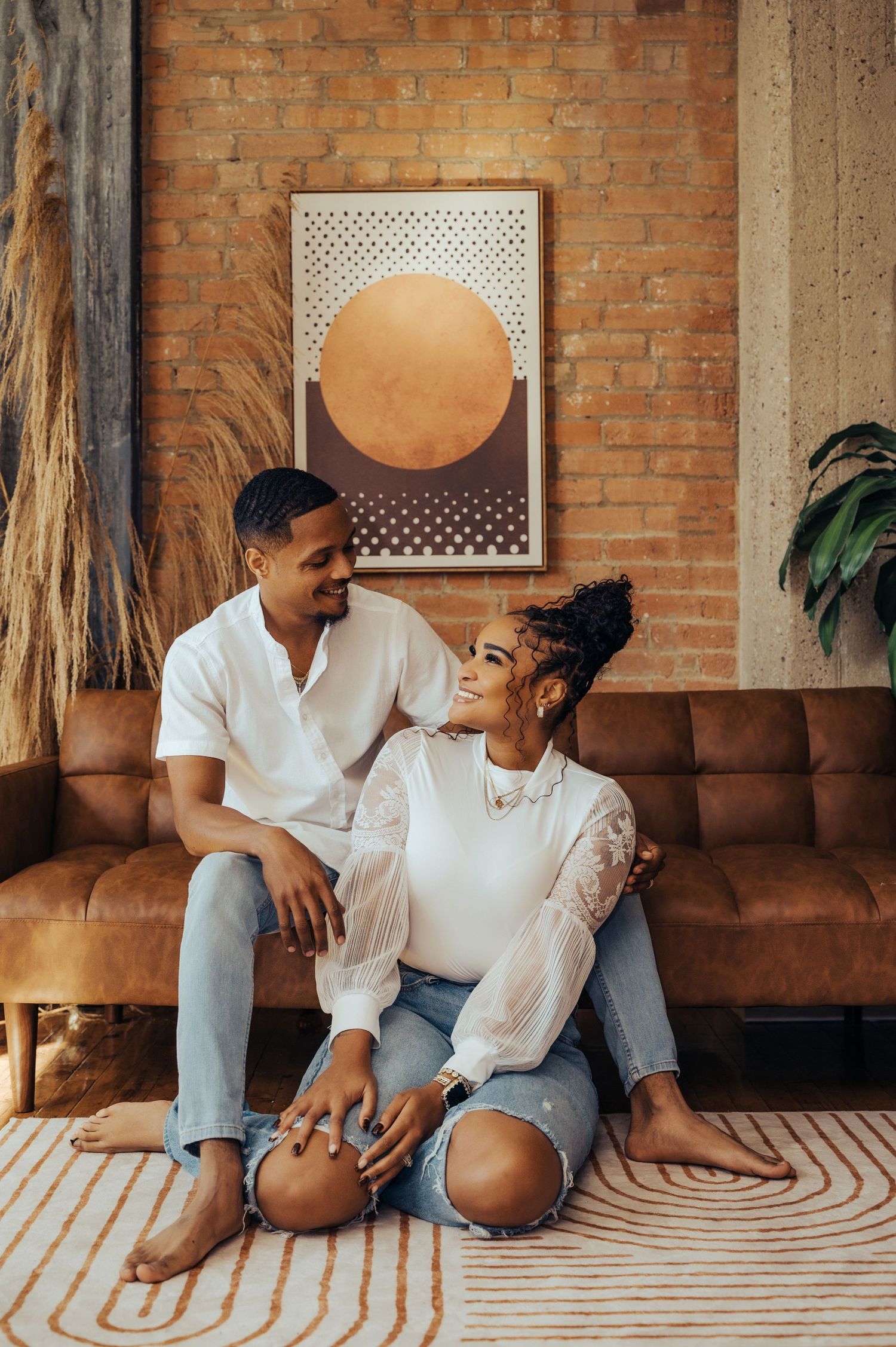 Couple sharing an intimate moment on a brown leather couch with geometric rug and modern wall art.
