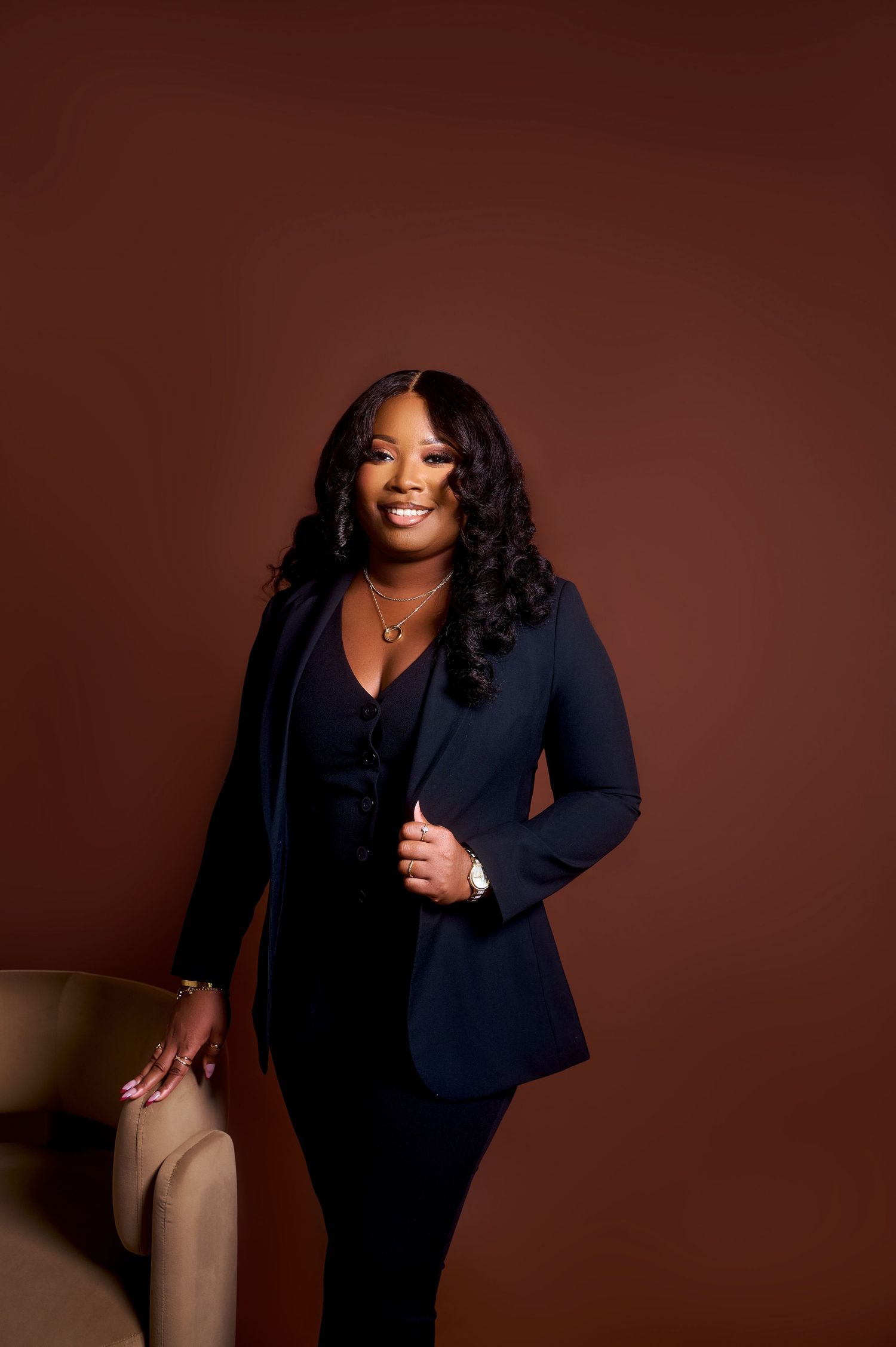Professional woman in navy blazer posing confidently against a warm brown studio background.