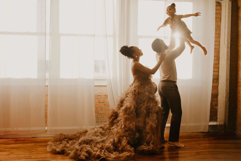 Silhouetted figures dance in sunlit room as woman in flowing dress twirls while someone lifts child overhead.