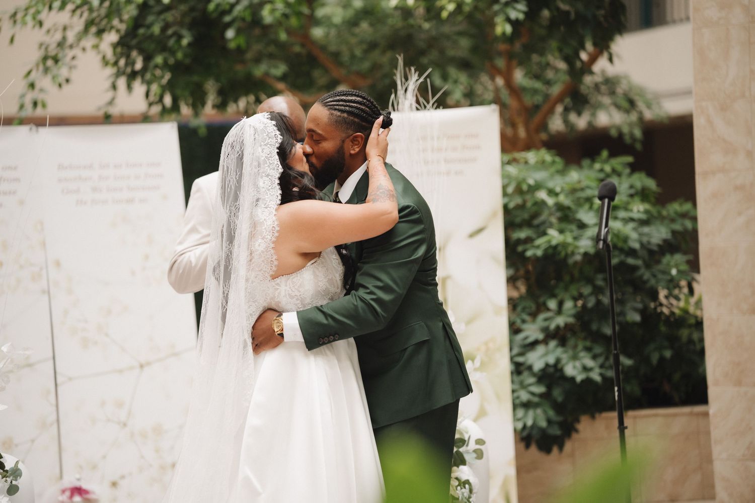 An interracial couple shares their first kiss as newlyweds during an outdoor wedding ceremony.
