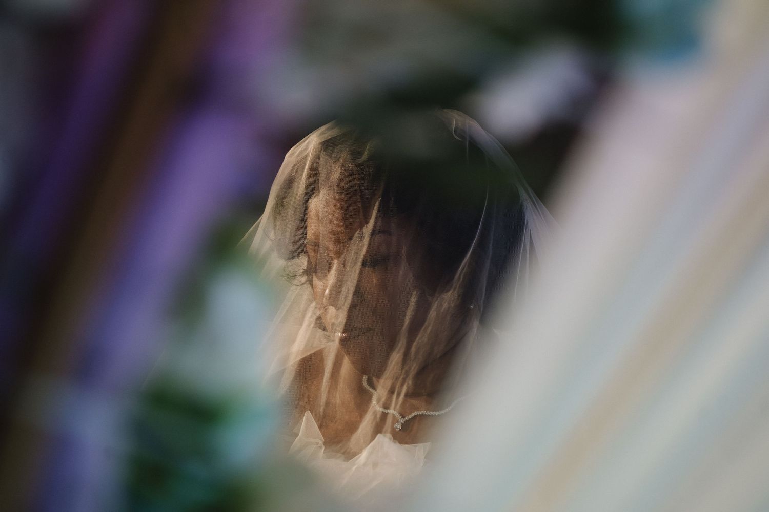 Artistic shot of bride through sheer wedding veil with soft bokeh background.