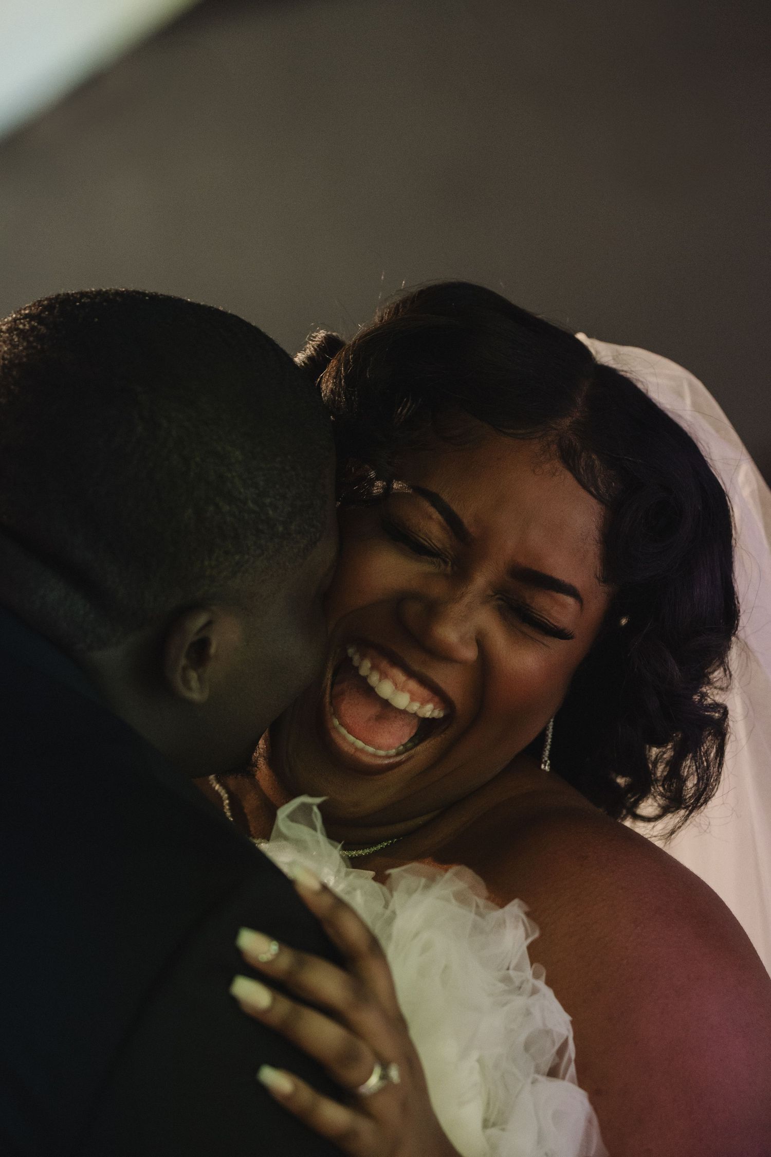Laughing bride in white veil embraces groom during joyful wedding moment.
